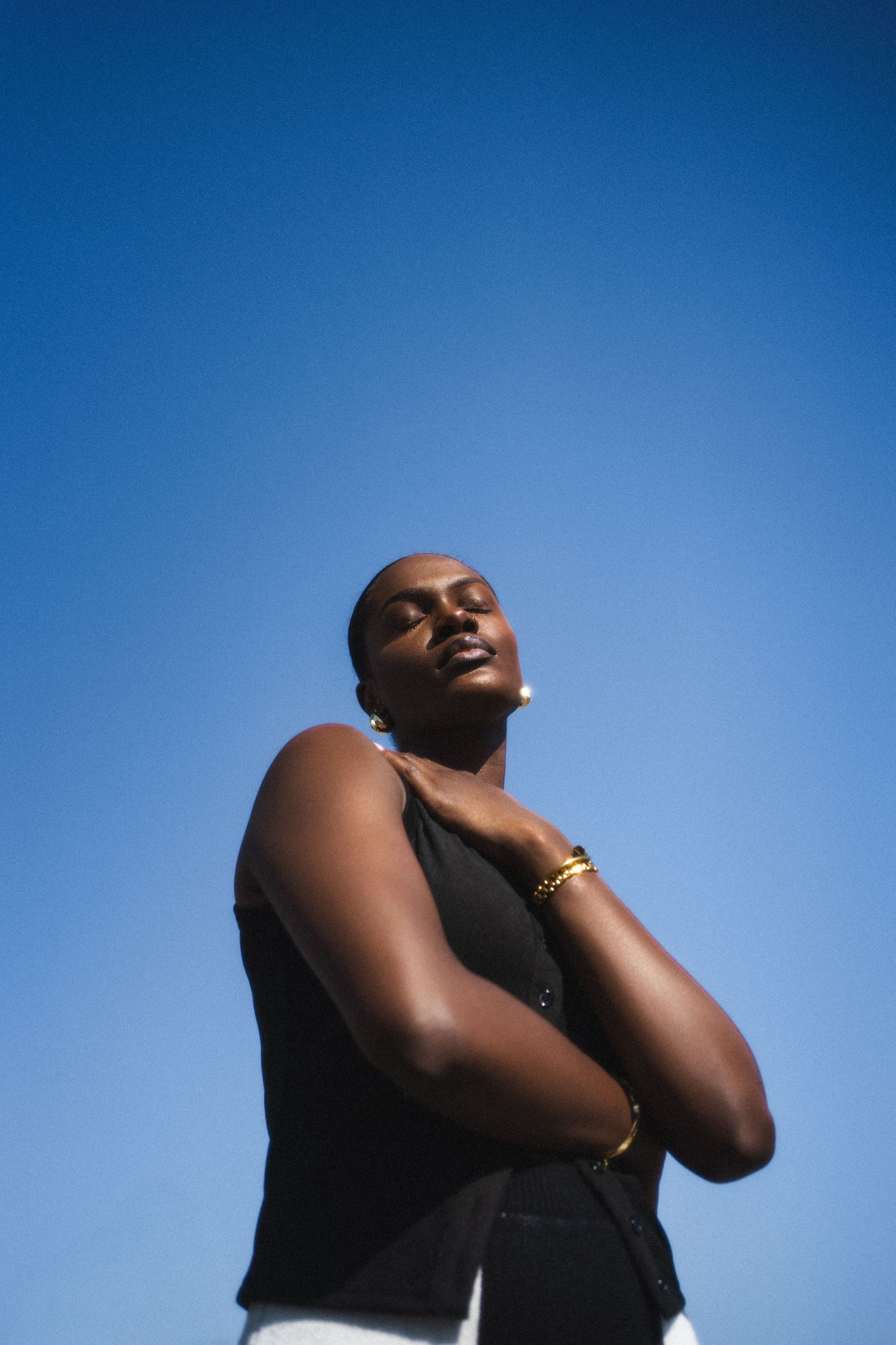 A person stands against a blue sky background with their head tilted back and eyes closed in a contemplative pose.