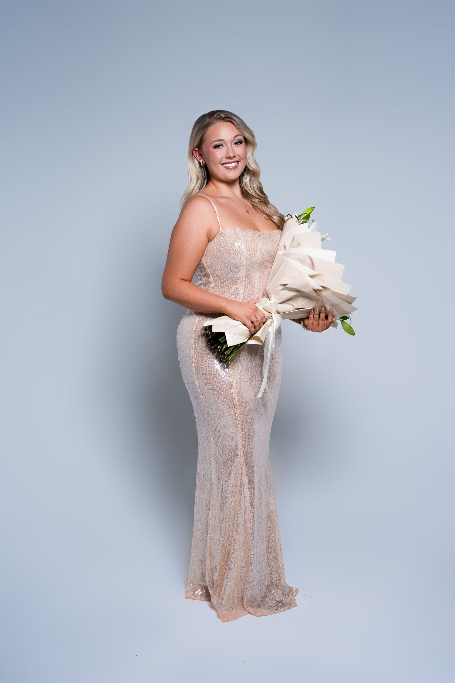 A person in a blush sequined cocktail dress poses elegantly against a light gray studio backdrop.
