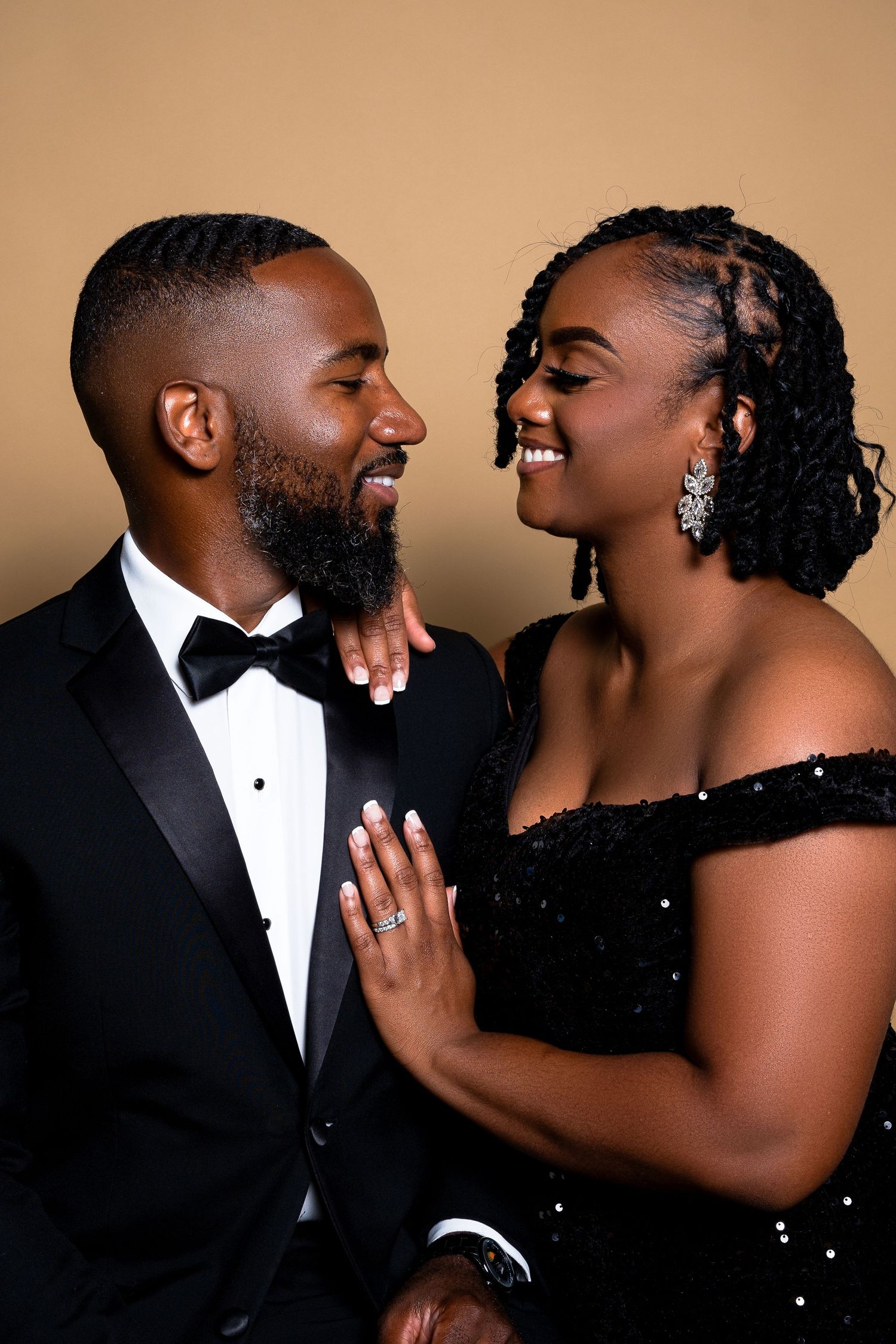 Intimate portrait of couple laughing together, wearing black formal wear against warm backdrop.