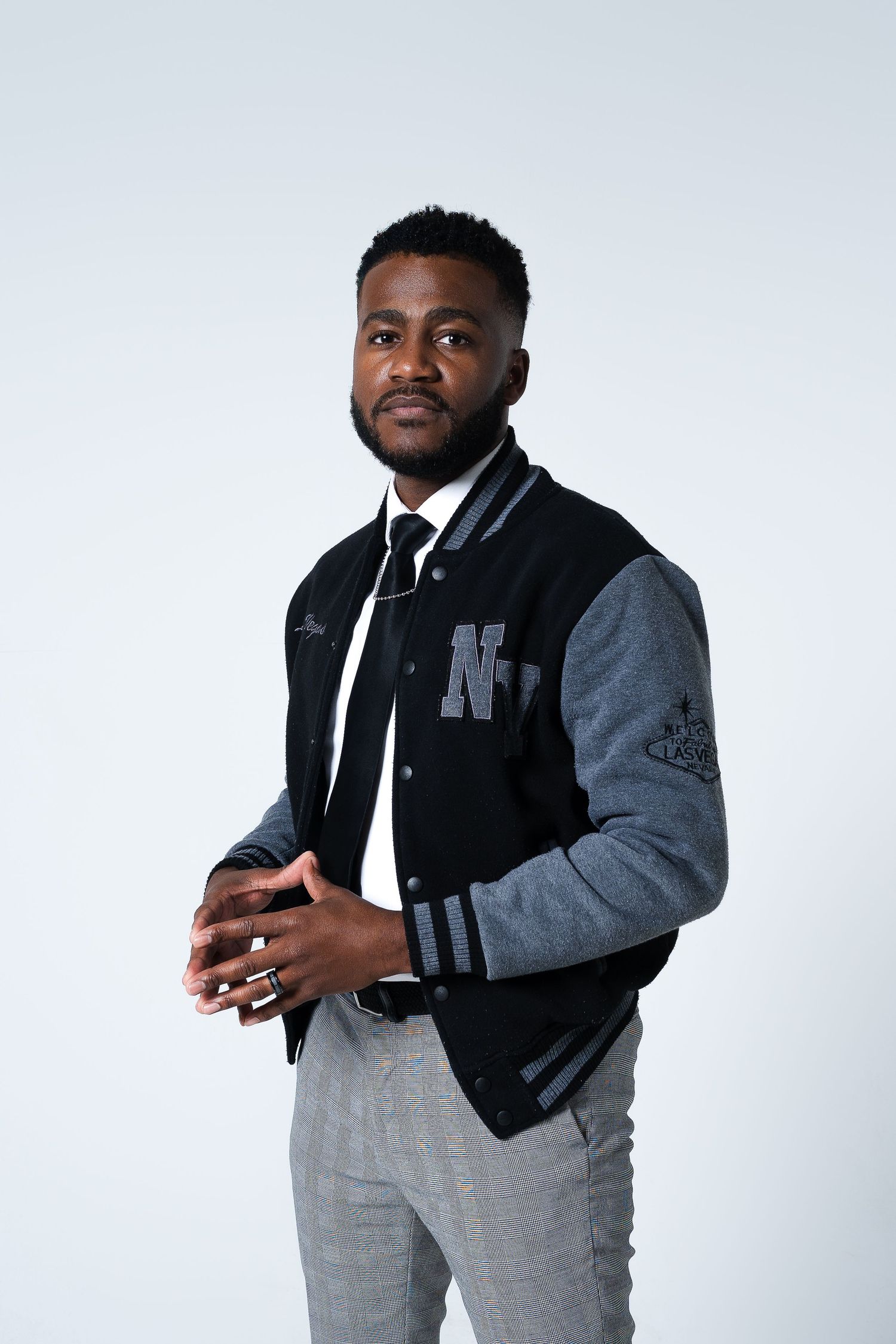 Athletic figure wearing two-tone letterman jacket poses in studio setting.