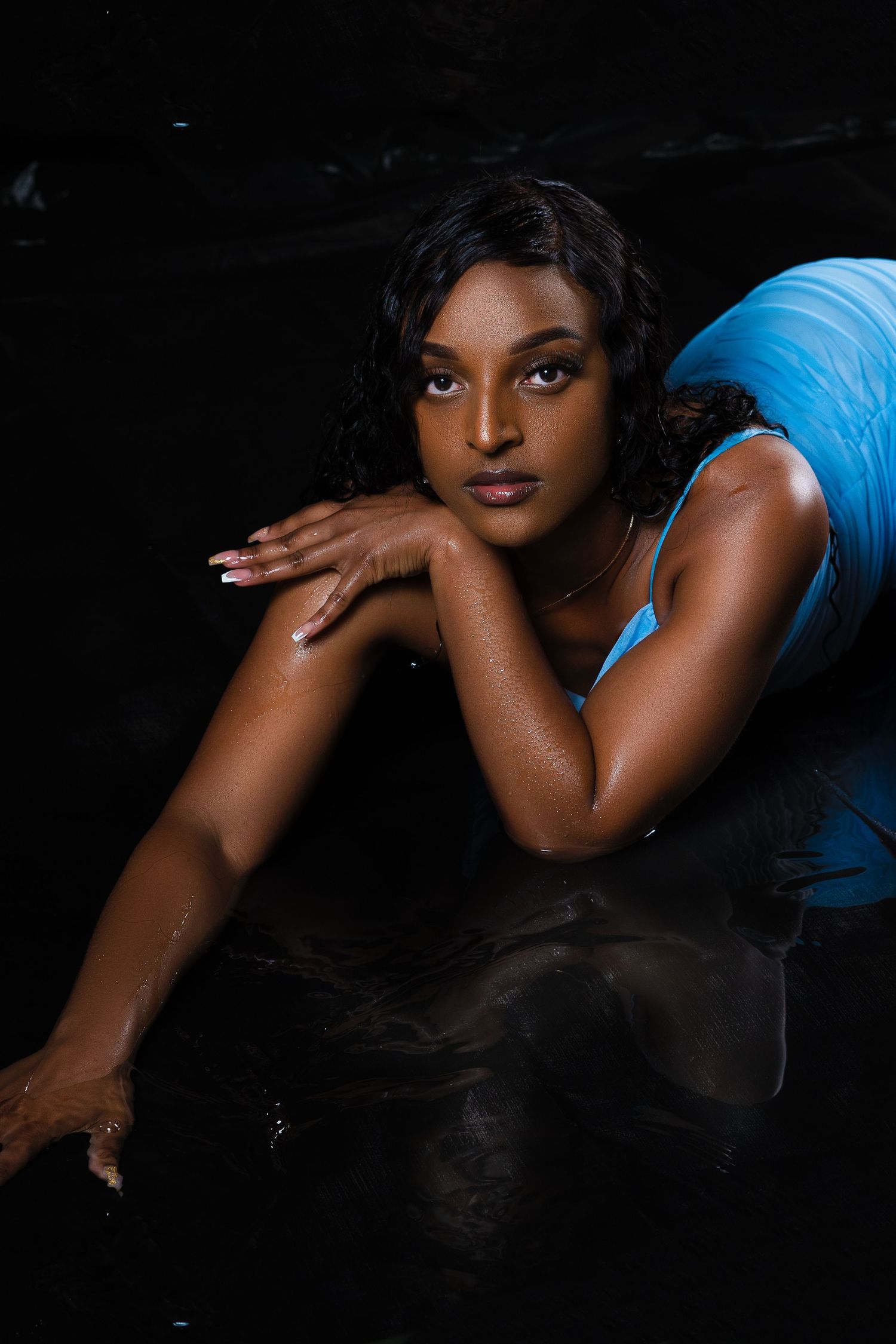 Woman in blue outfit poses elegantly against dark background.