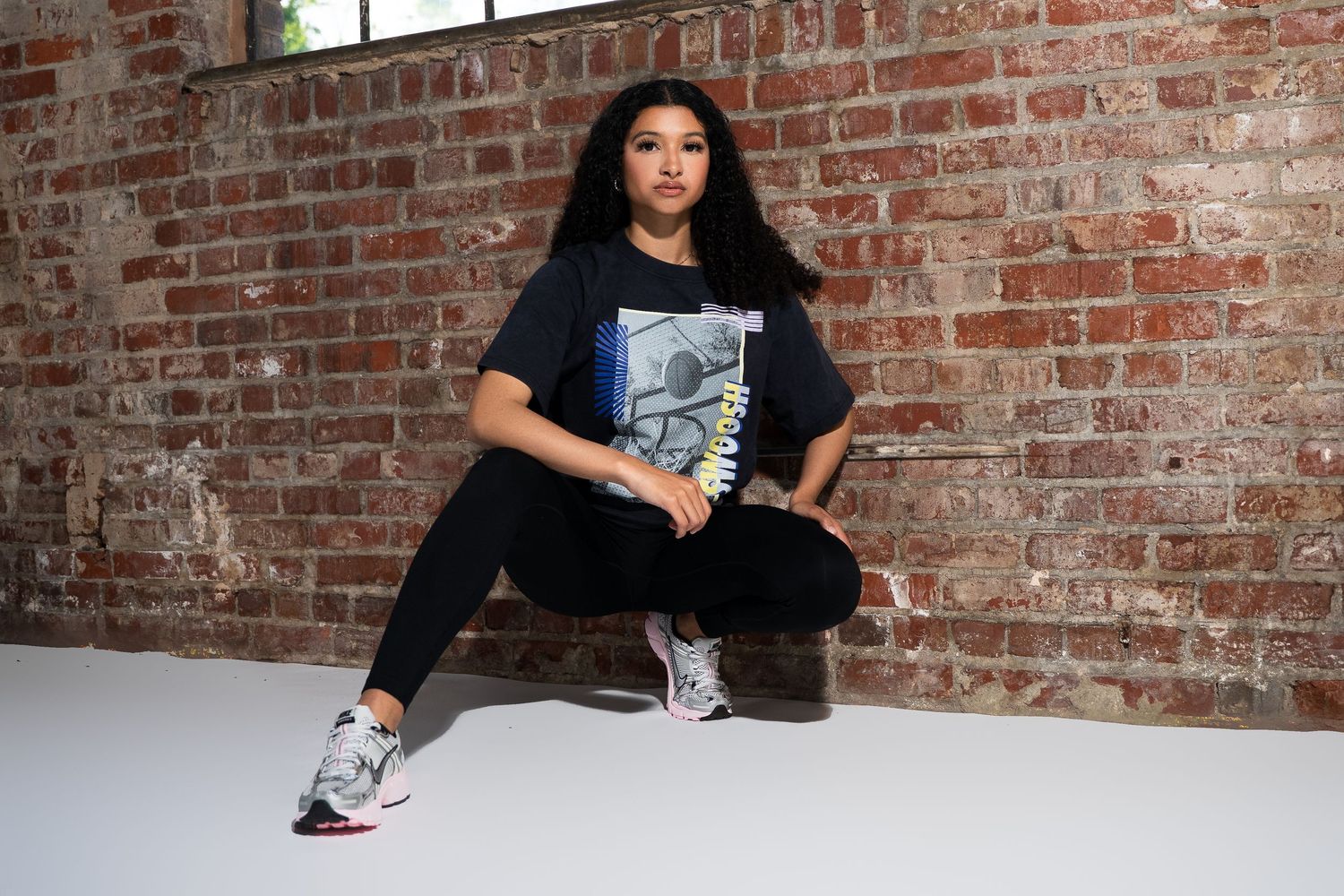 Casual streetwear look with graphic t-shirt and sneakers against brick wall background.