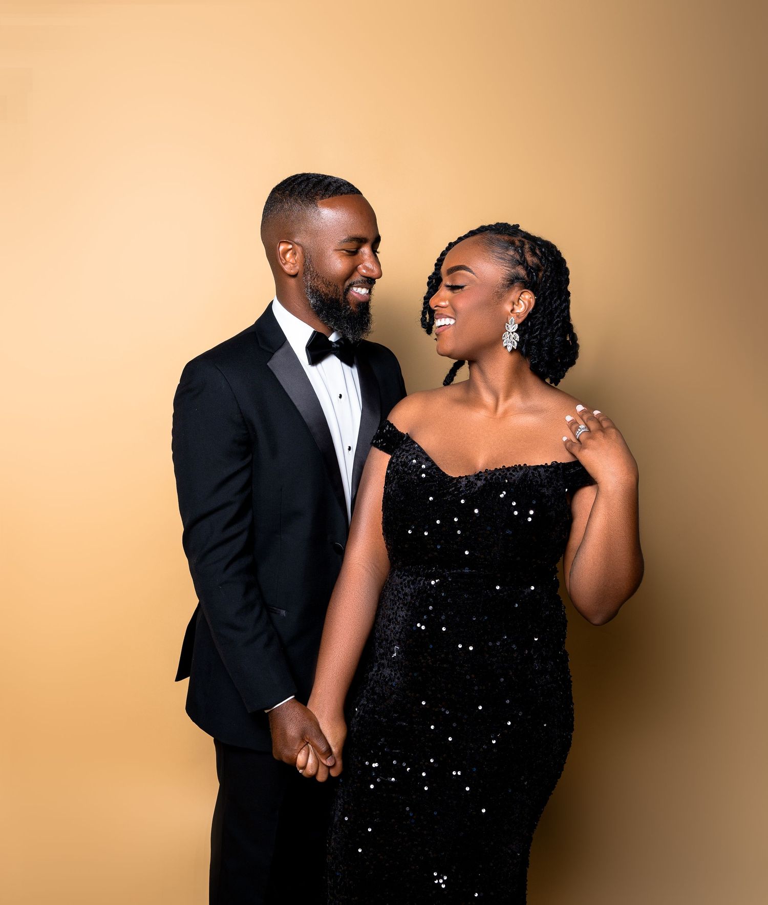 Elegant couple shares a joyful moment together wearing formal attire against a warm beige background.