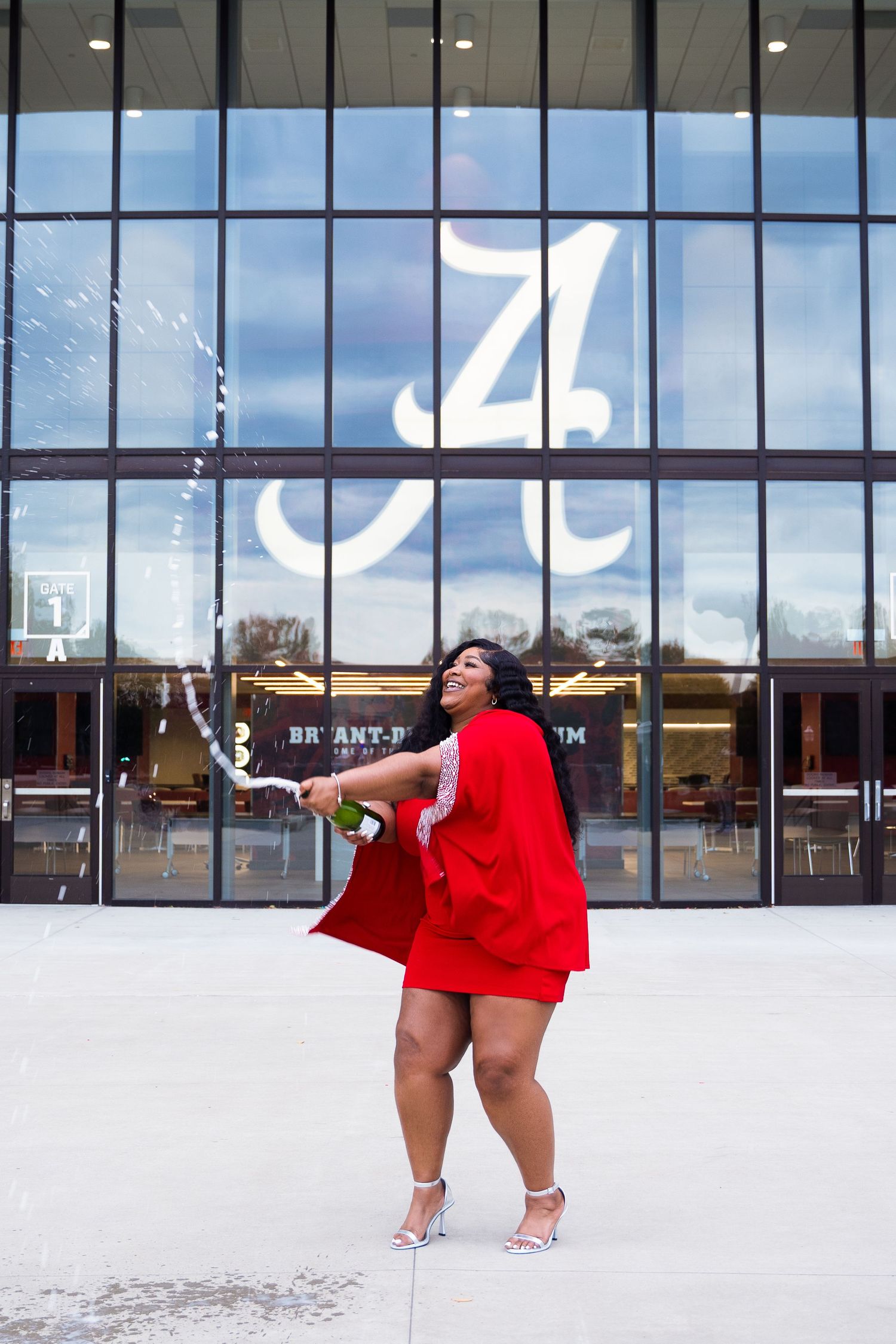 Joyful pose in red cape dress with spinning motion against glass building facade.