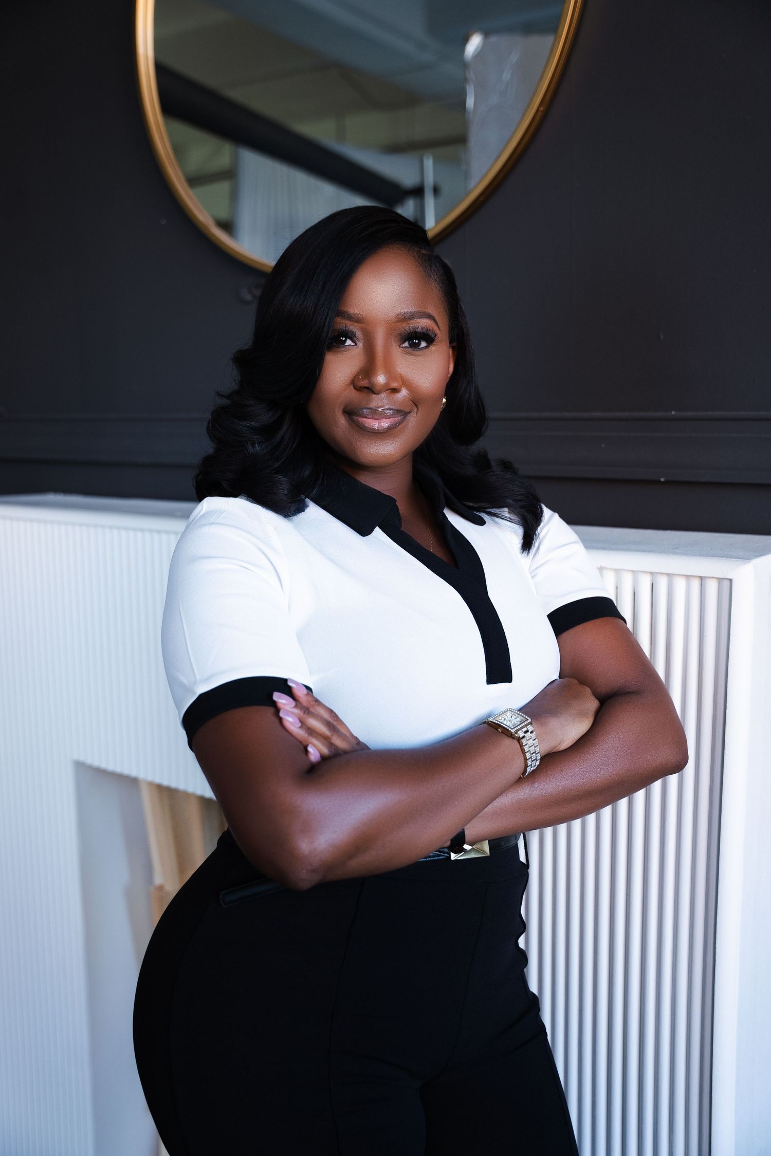 Confident businesswoman in white and black outfit poses with crossed arms in modern office setting.