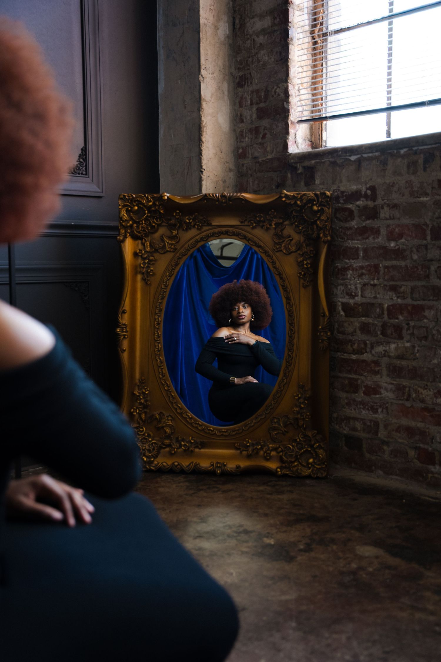Ornate gold frame on exposed brick wall displays blue portrait in dramatic lighting and moody atmosphere.