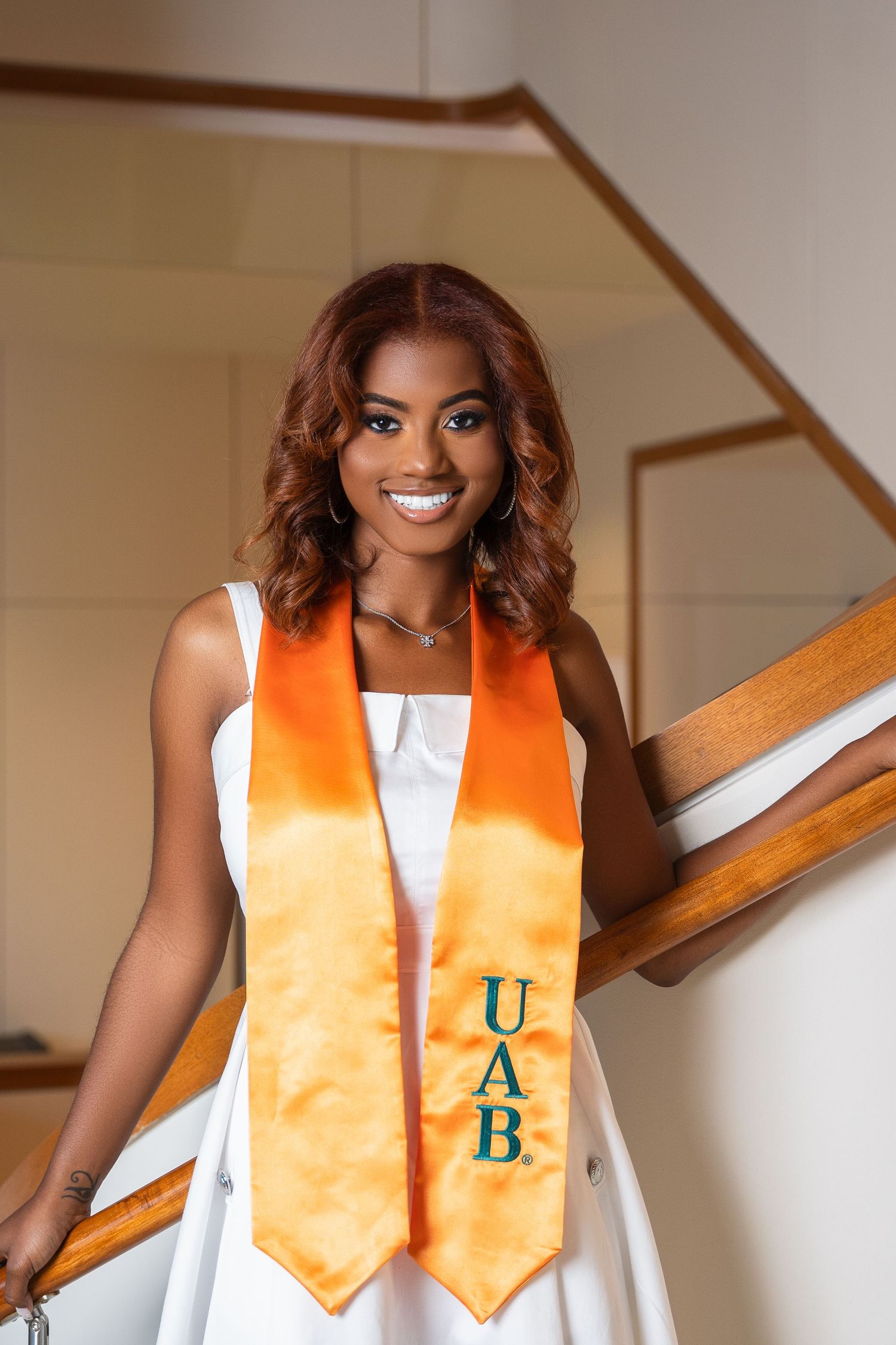 Graduate wearing orange and white graduation stole poses on staircase.