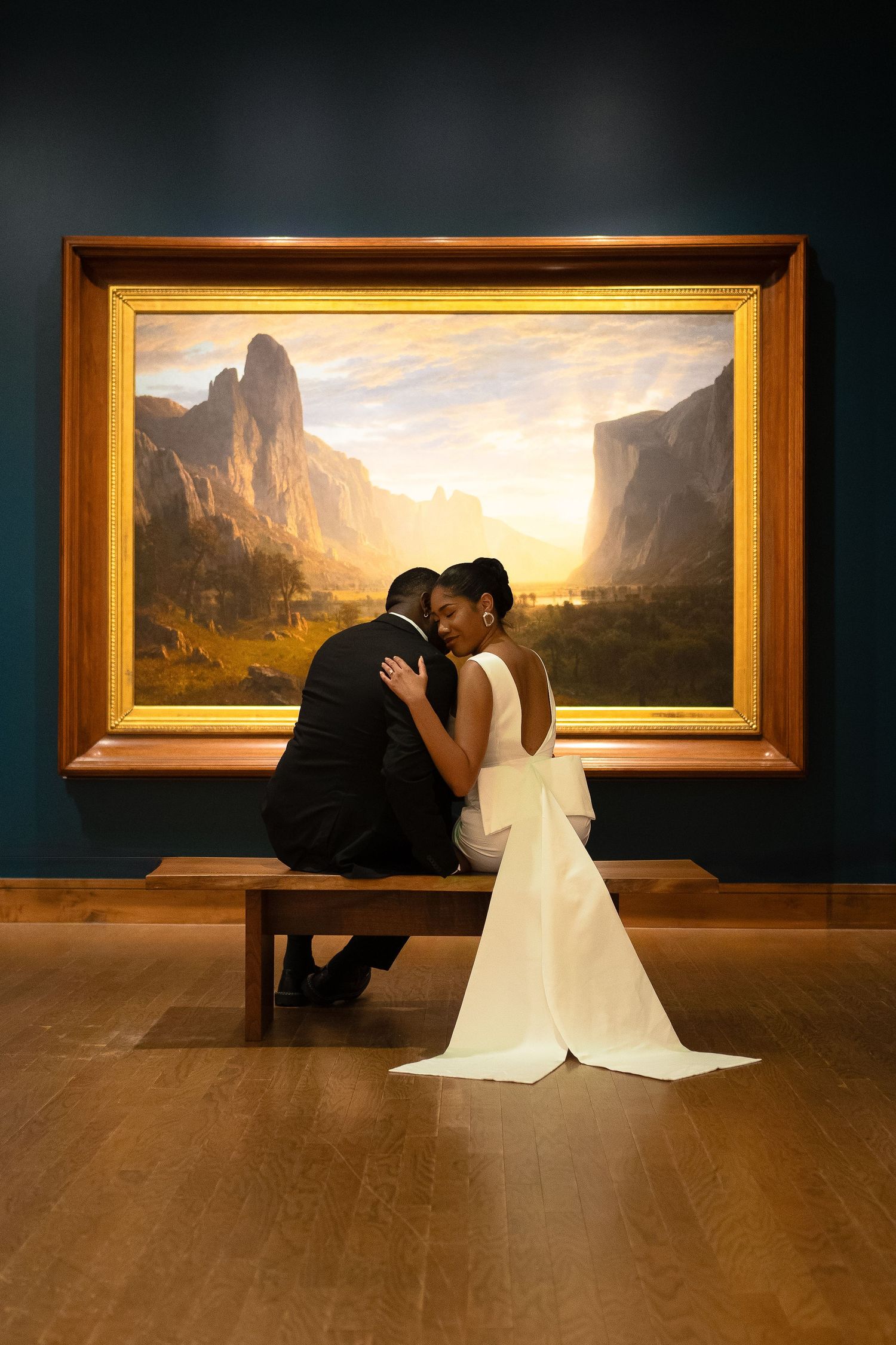 Romantic wedding photo of couple sitting before landscape painting in art gallery.
