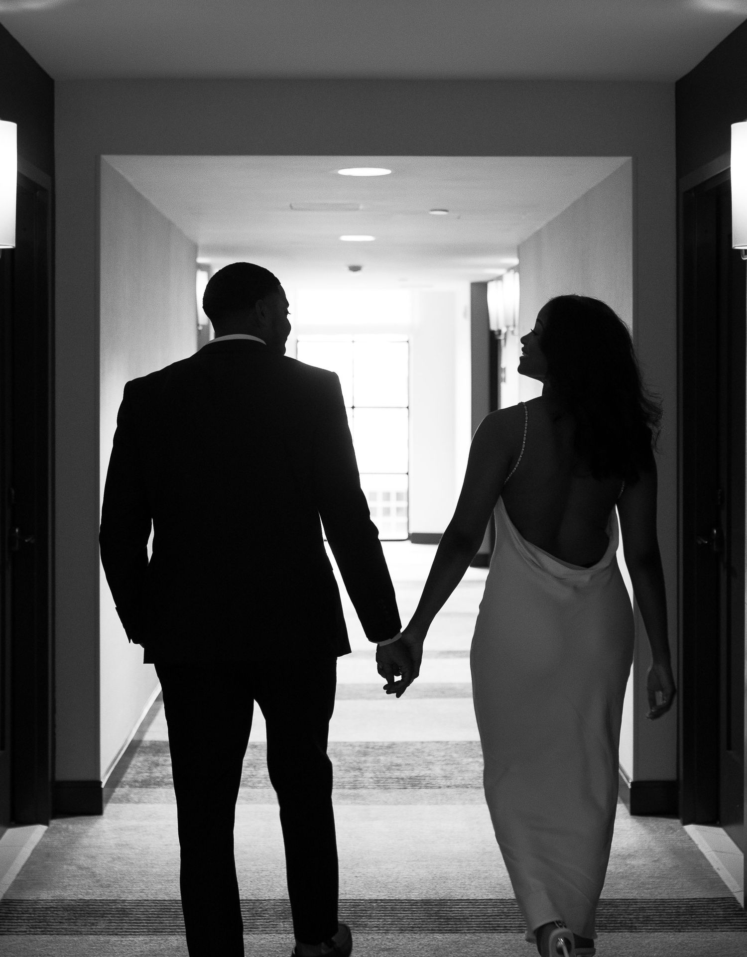 A silhouette of a couple holding hands while walking down a hallway.