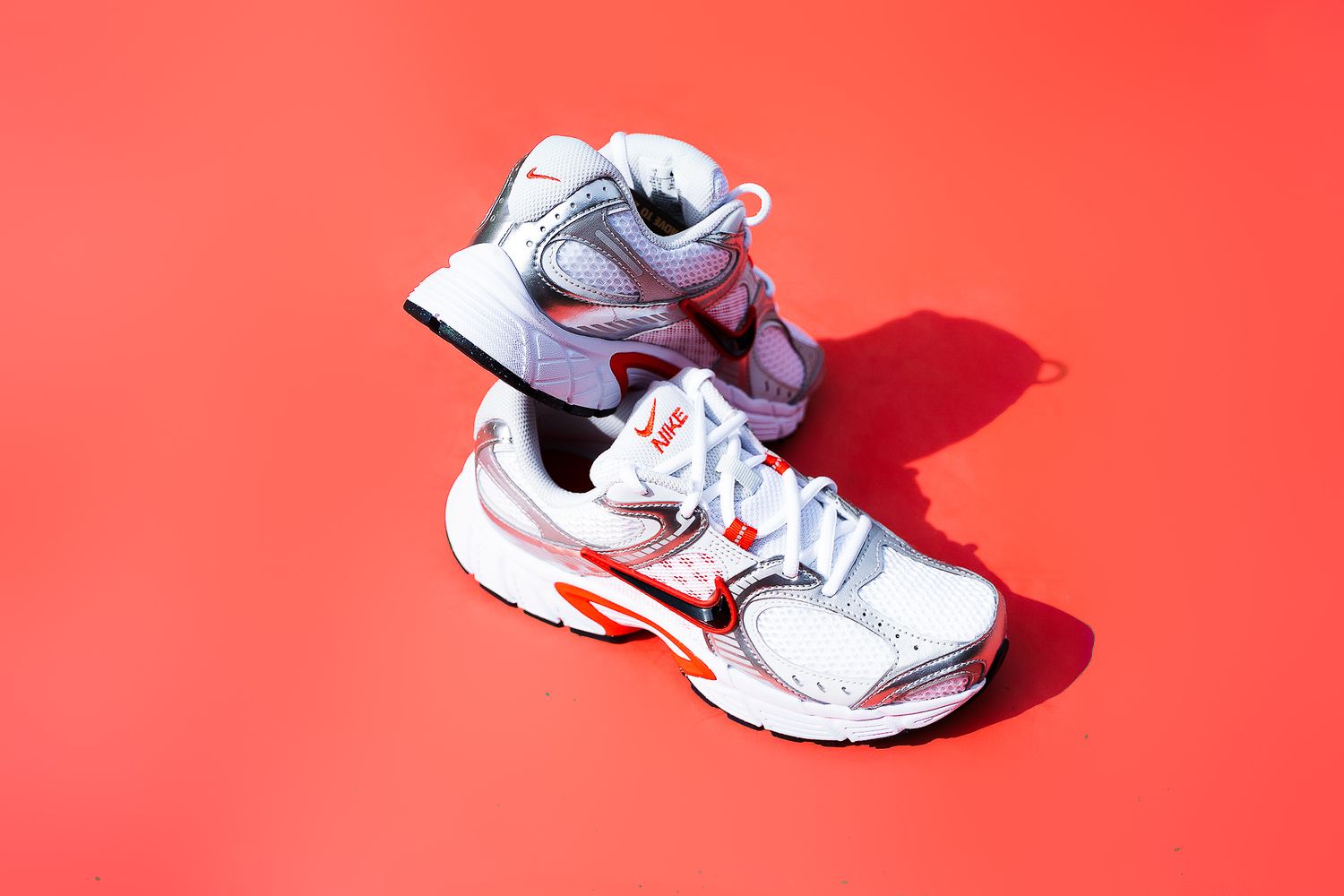 White athletic sneaker casting shadow on bright red background.