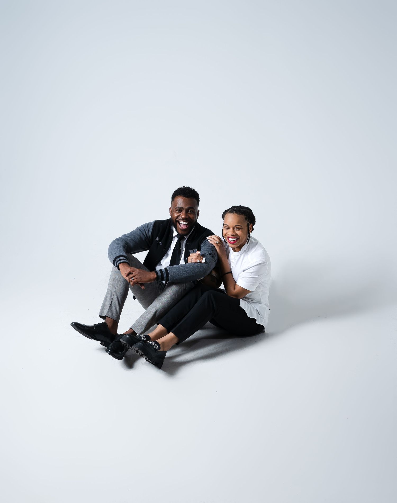 A playful portrait of two people sitting and laughing together on a white backdrop.