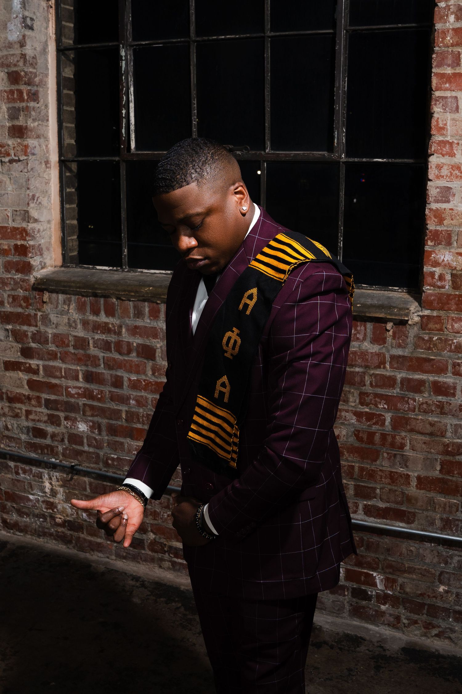 Fashion portrait in moody industrial setting with brick walls and window lighting.