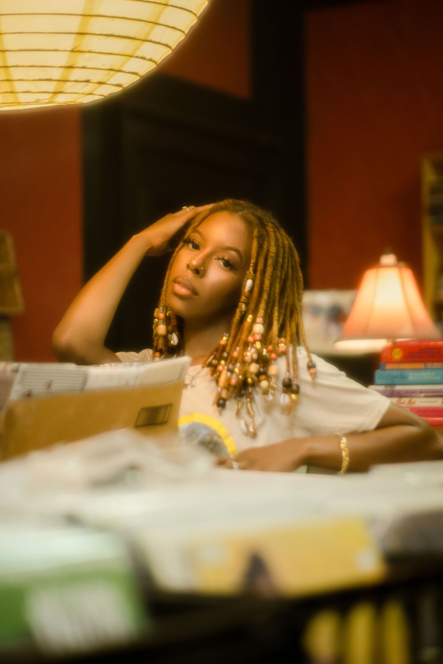Dreamy vintage-style portrait with beaded hair under warm lamp light.