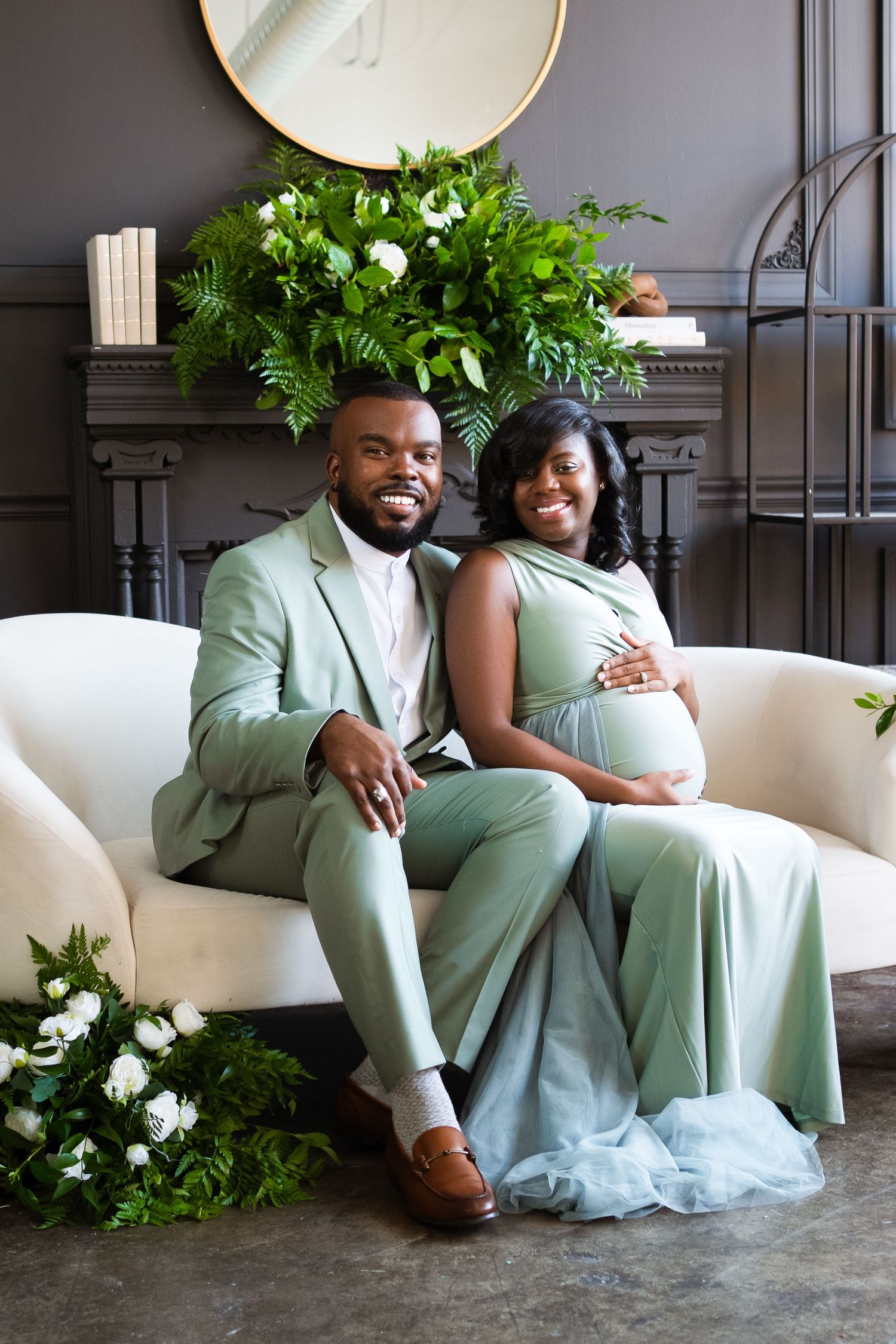 Romantic wedding couple in mint green attire poses together on white seating with decorative plants.