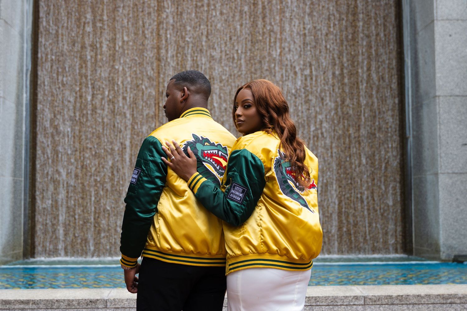 A couple wearing matching yellow varsity jackets posing together against a textured wall.
