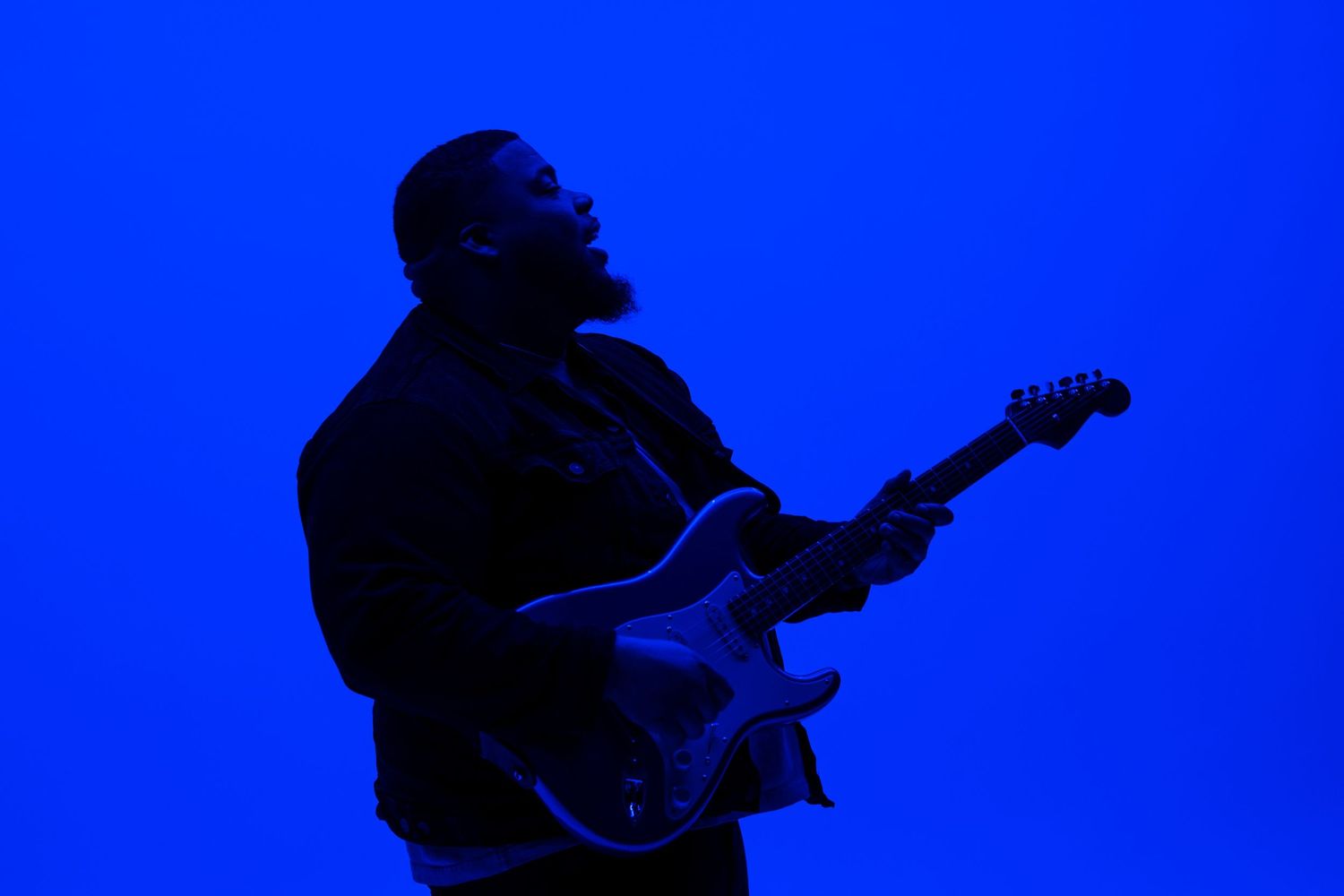 Silhouette of musician playing electric guitar against vibrant blue backdrop.