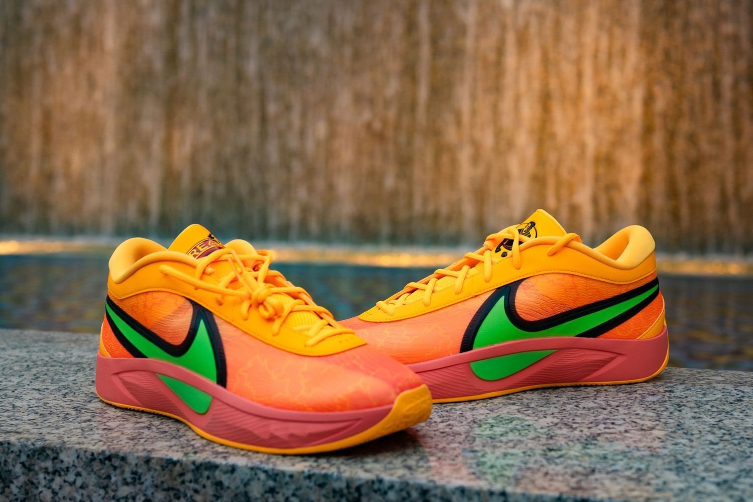 Bright orange and pink Nike sneakers with green swoosh photographed on concrete surface.