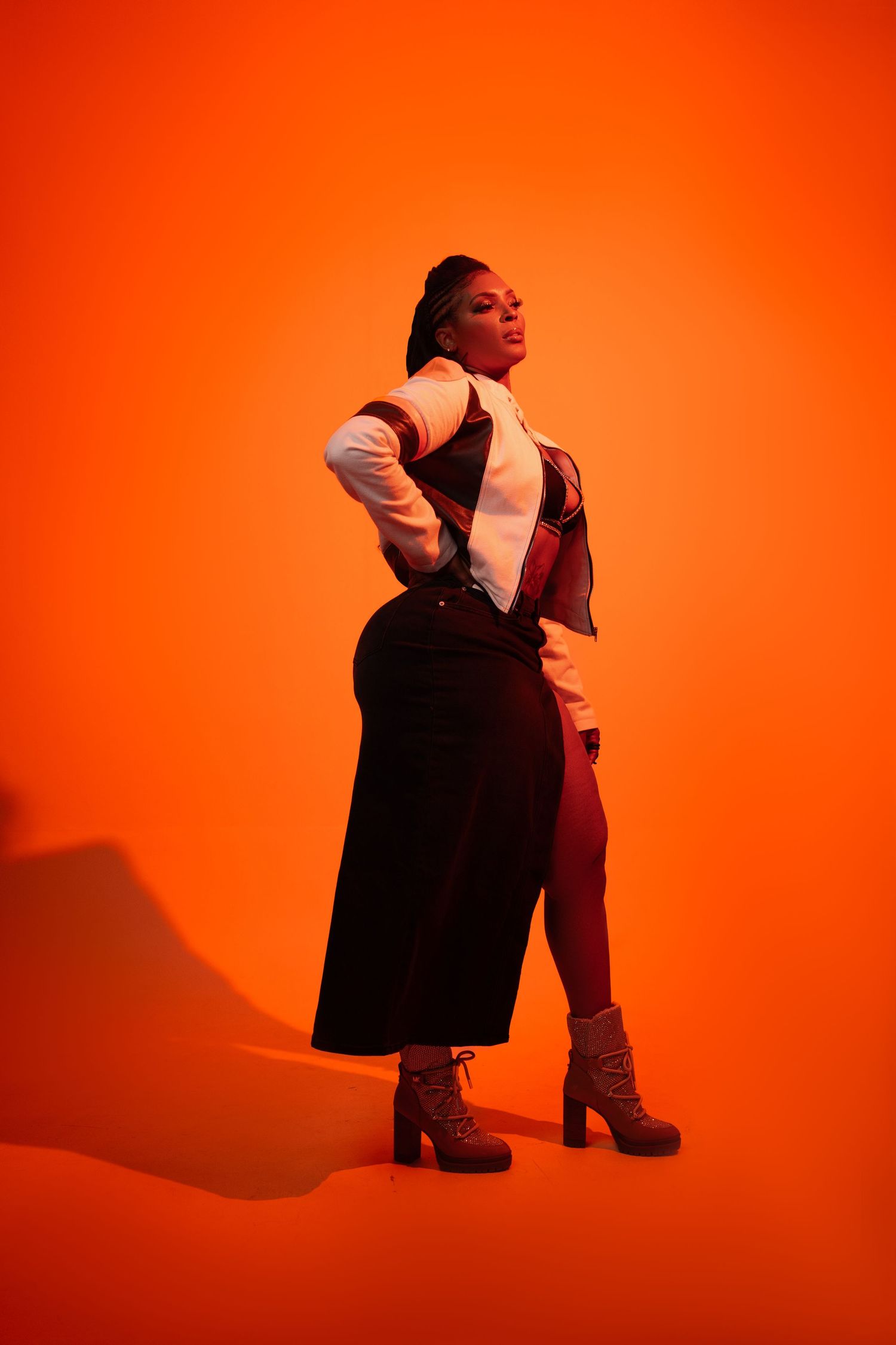 Fashion portrait against vibrant orange background with platform boots and dramatic pose.