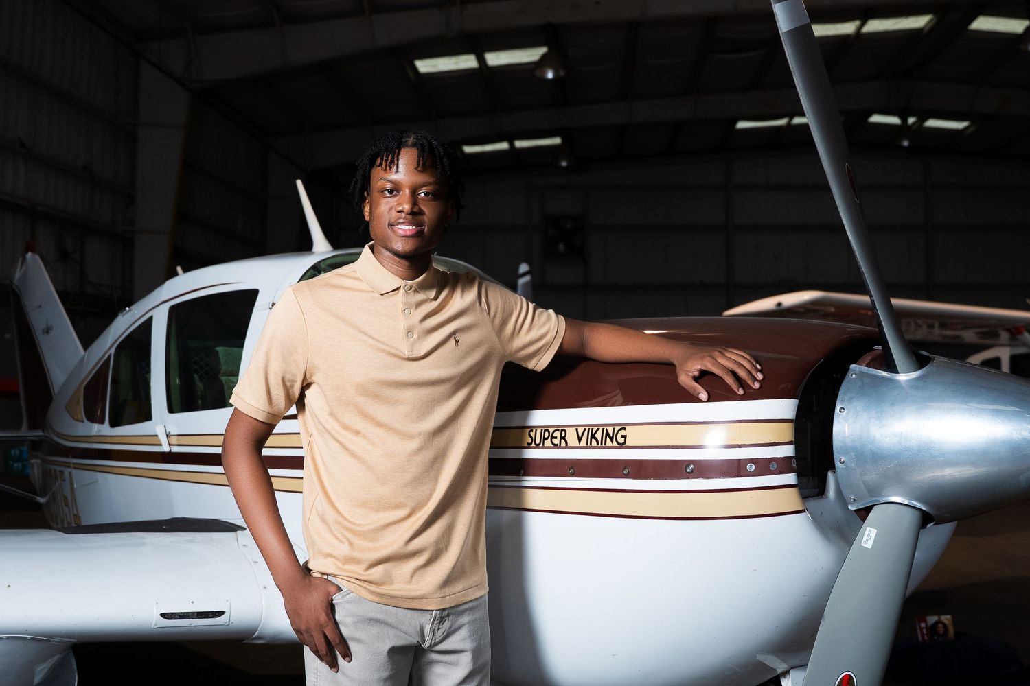 Young aviator standing confidently next to a small private aircraft in a hangar.