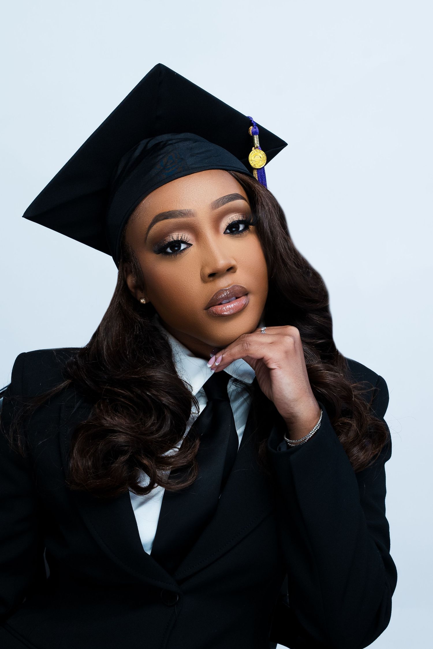 Professional graduation portrait in black cap, gown and tie against white background.