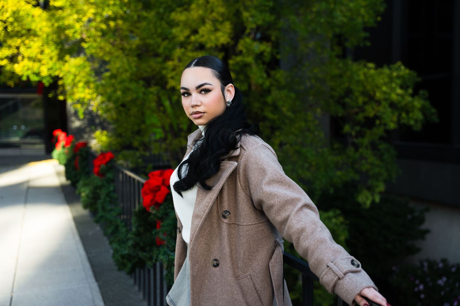 A person in a brown coat poses outdoors against a green foliage background in autumn.
