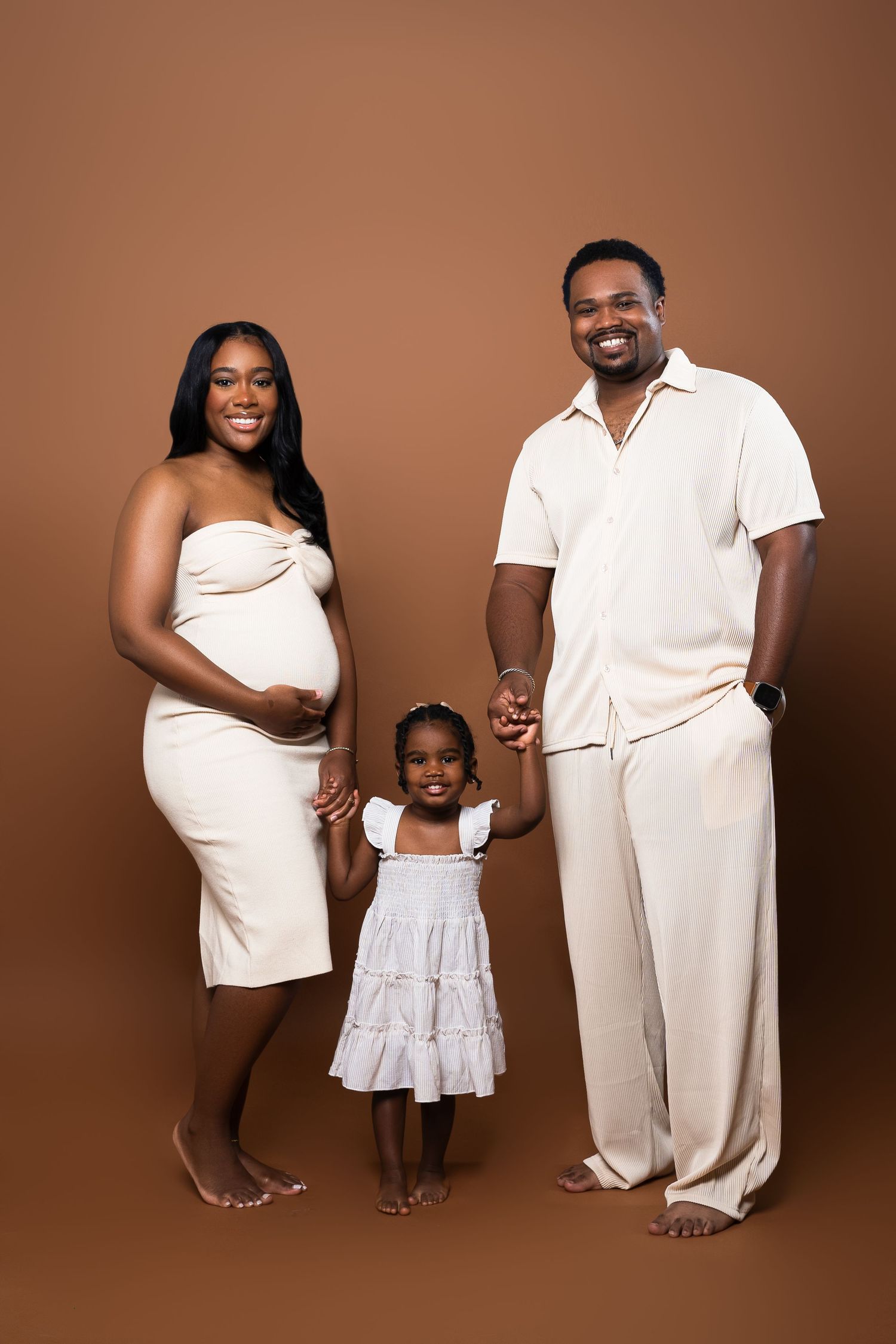 A family portrait in all white clothing against a brown backdrop.