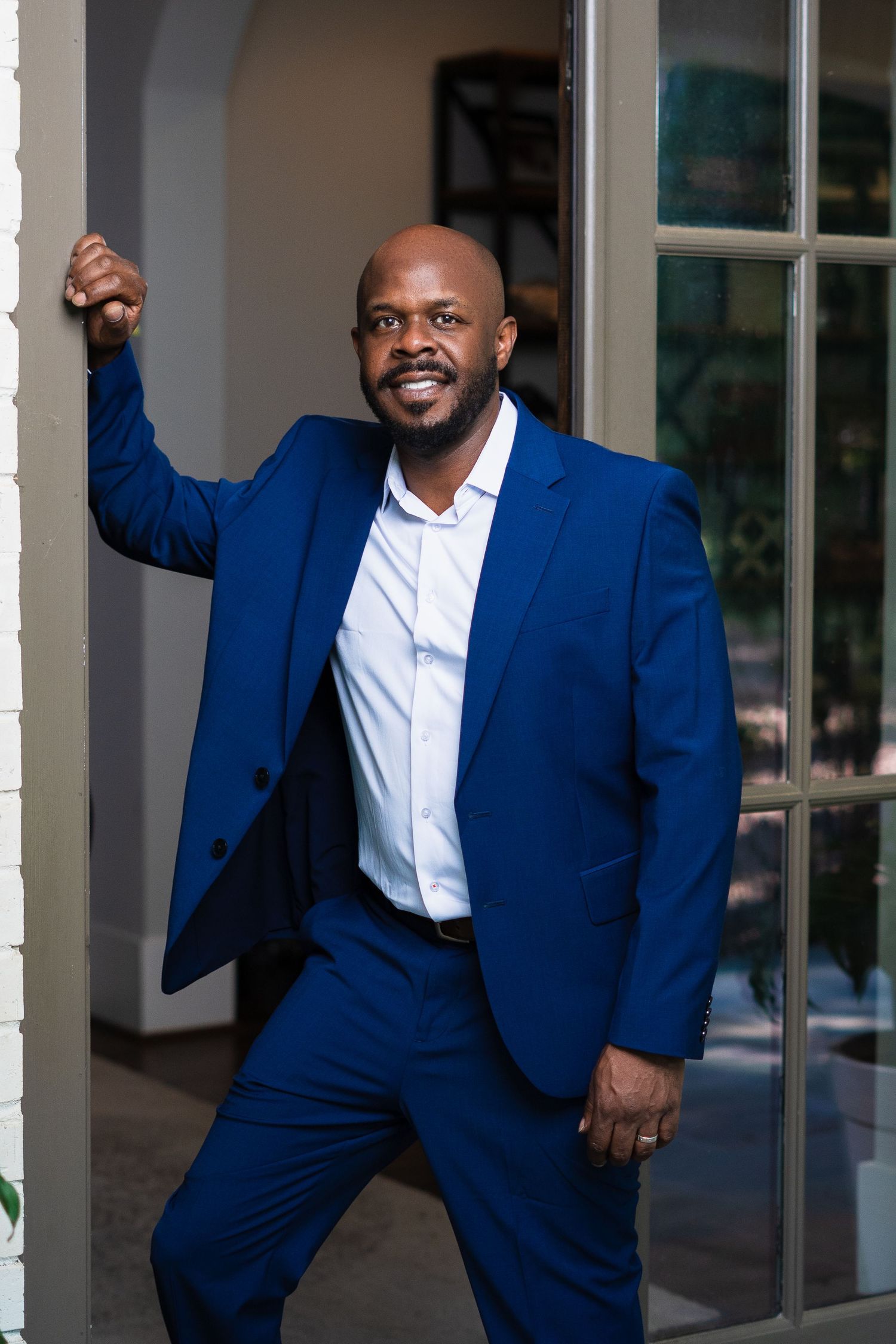 Professional portrait in navy blue suit standing by glass doors.