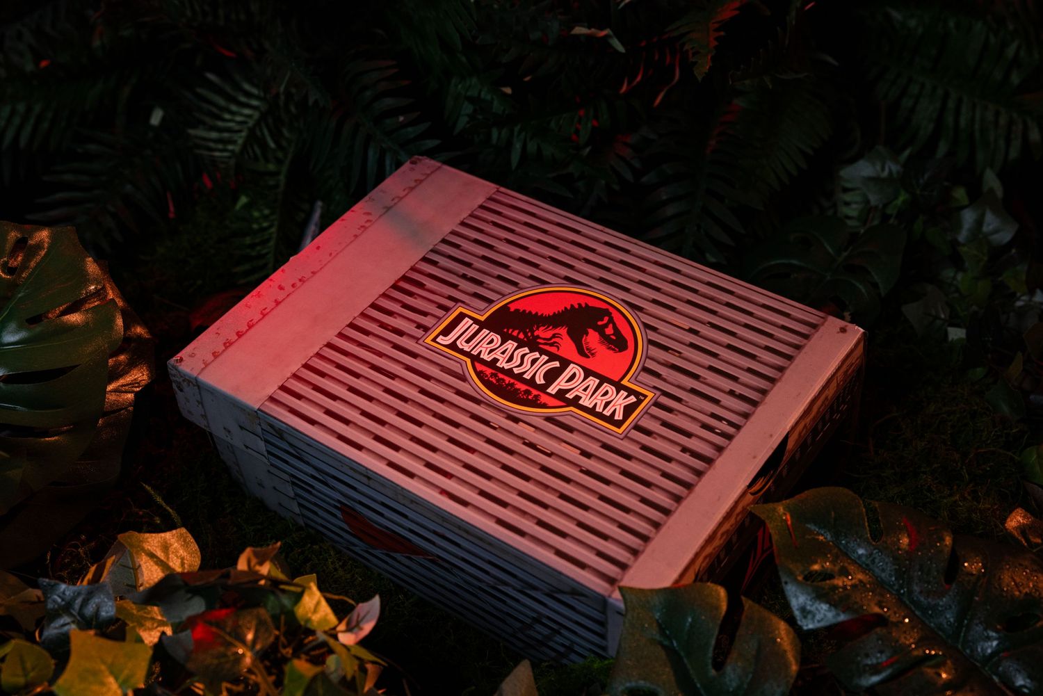 Jurassic Park branded console displayed among tropical leaves with dramatic red lighting.