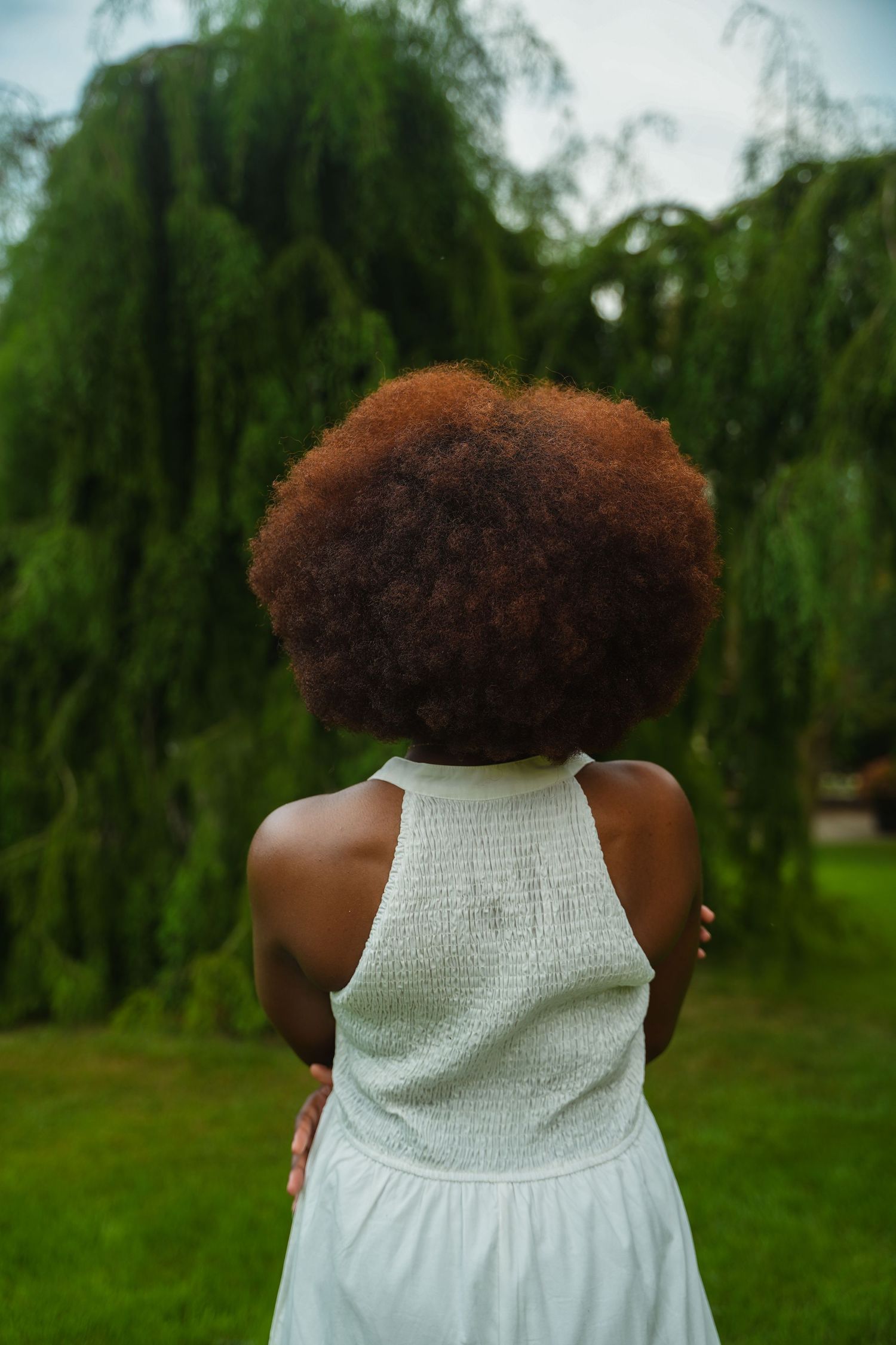 A sequence of photos showing a person with natural curly hair wearing a white sleeveless dress against a green outdoor background.