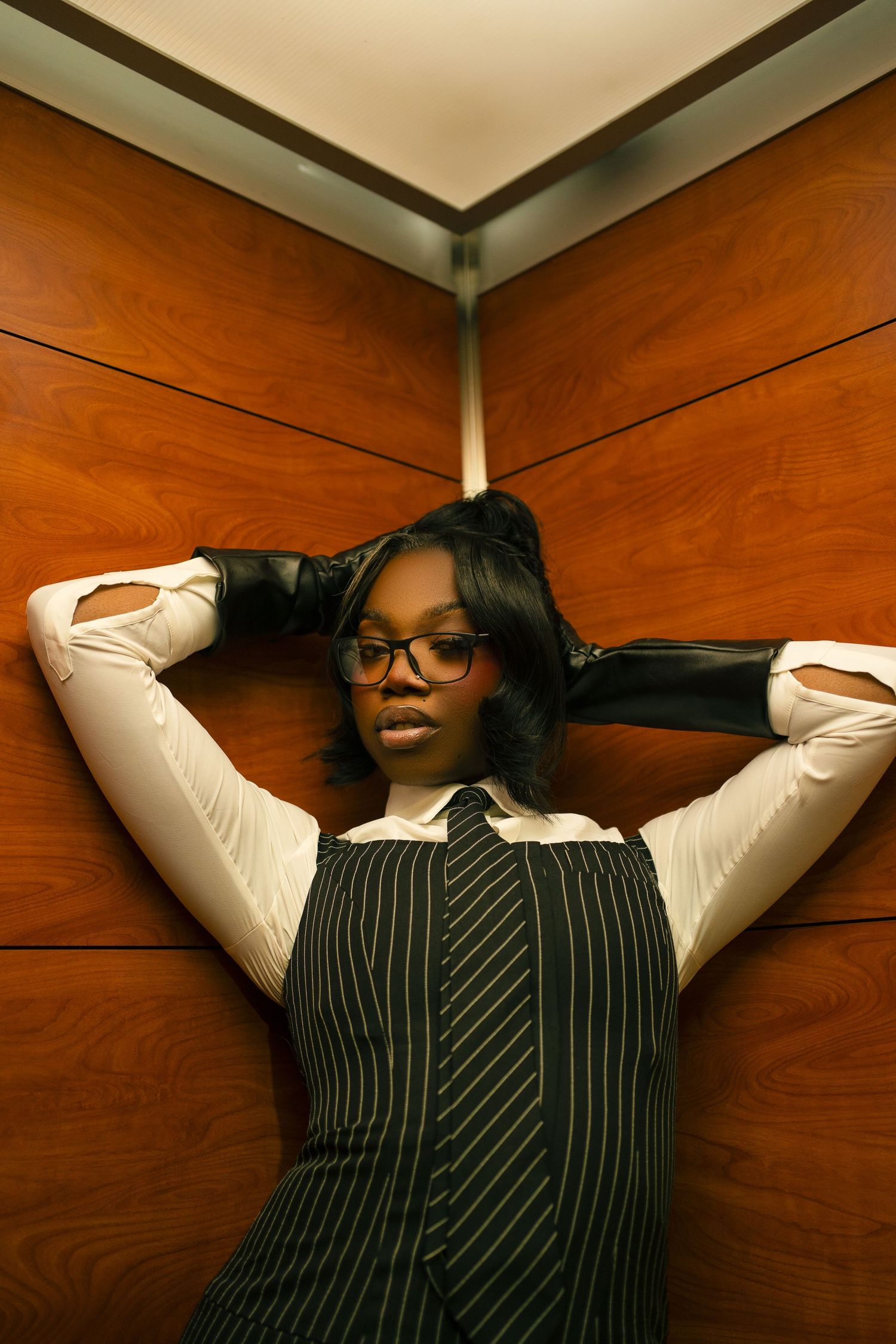 A person in a pinstriped blazer leans back against a wood paneled wall in a sequence of progressive poses.