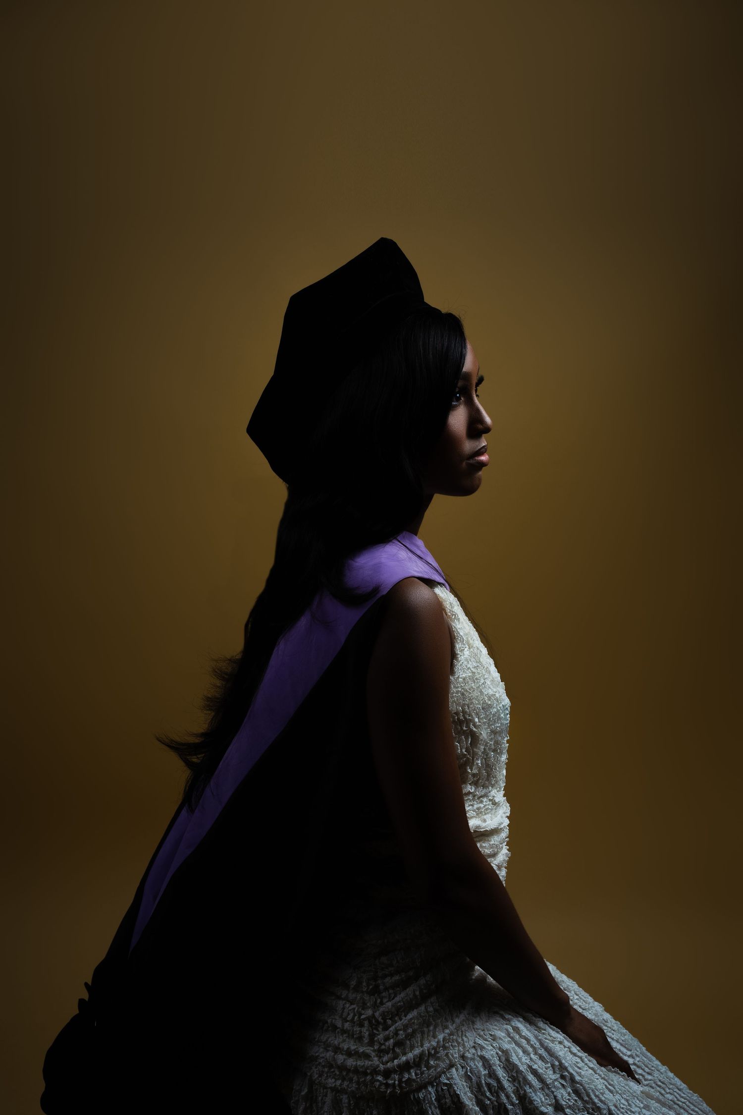 Dramatic side profile silhouette in white lace dress and black head covering against dark brown background.
