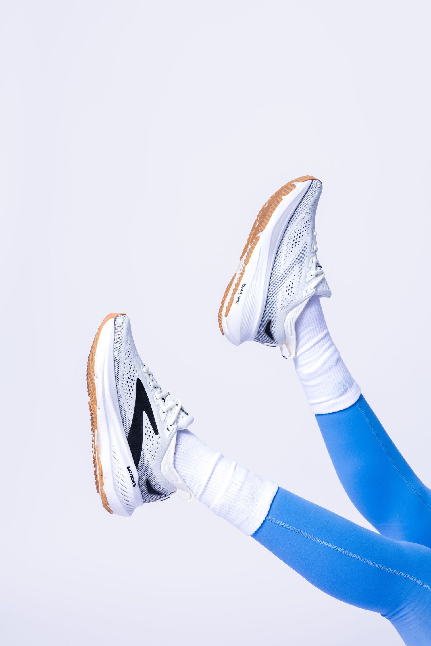 Person wearing blue leggings, white socks, and gray athletic sneakers with gum soles against a white background.