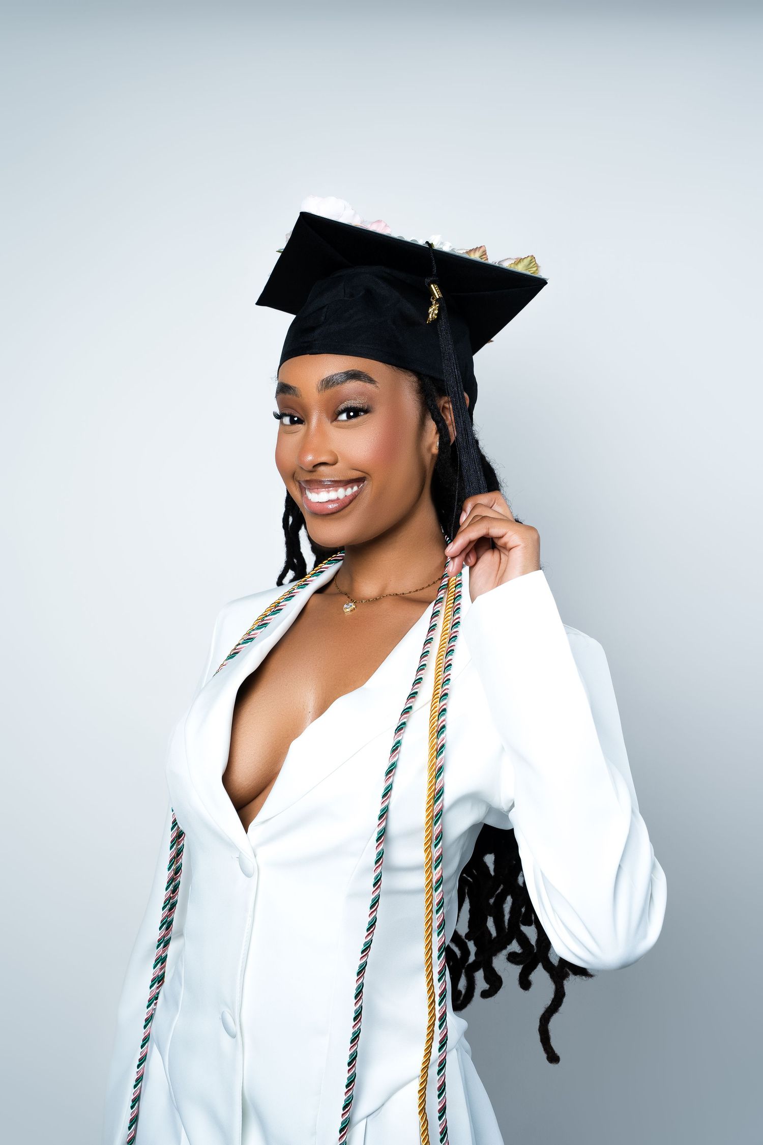 Graduate in white academic regalia and cap poses for a series of celebratory graduation portraits against a light background.