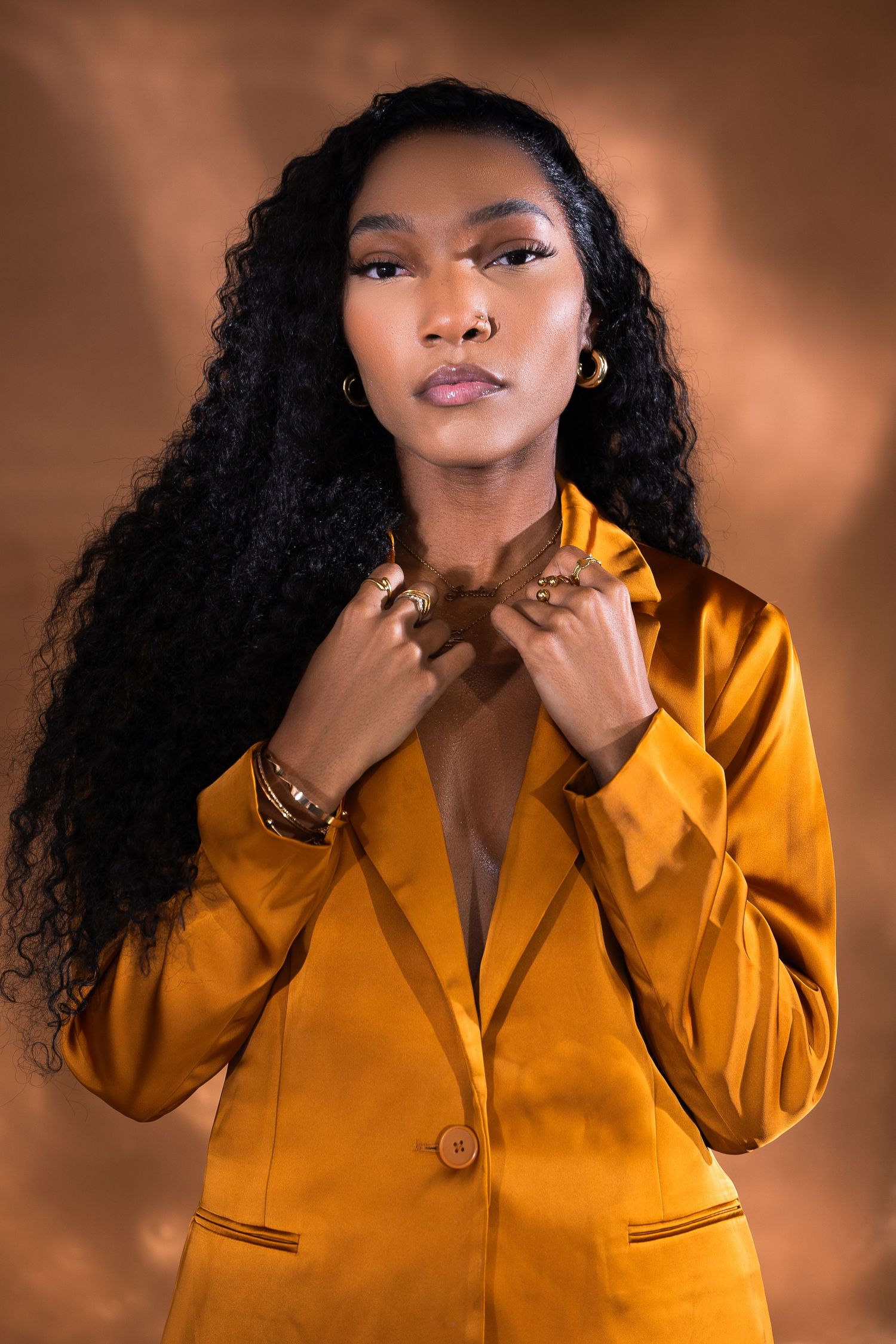 Fashion portrait in gold blazer against warm brown background.