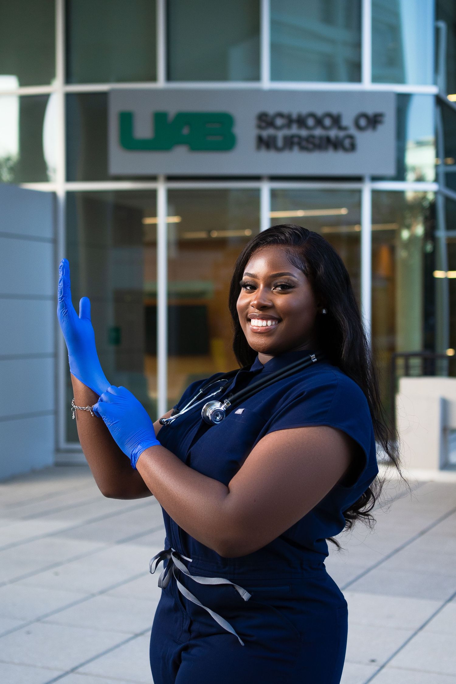 Healthcare professional wearing blue medical gloves outside nursing school building.