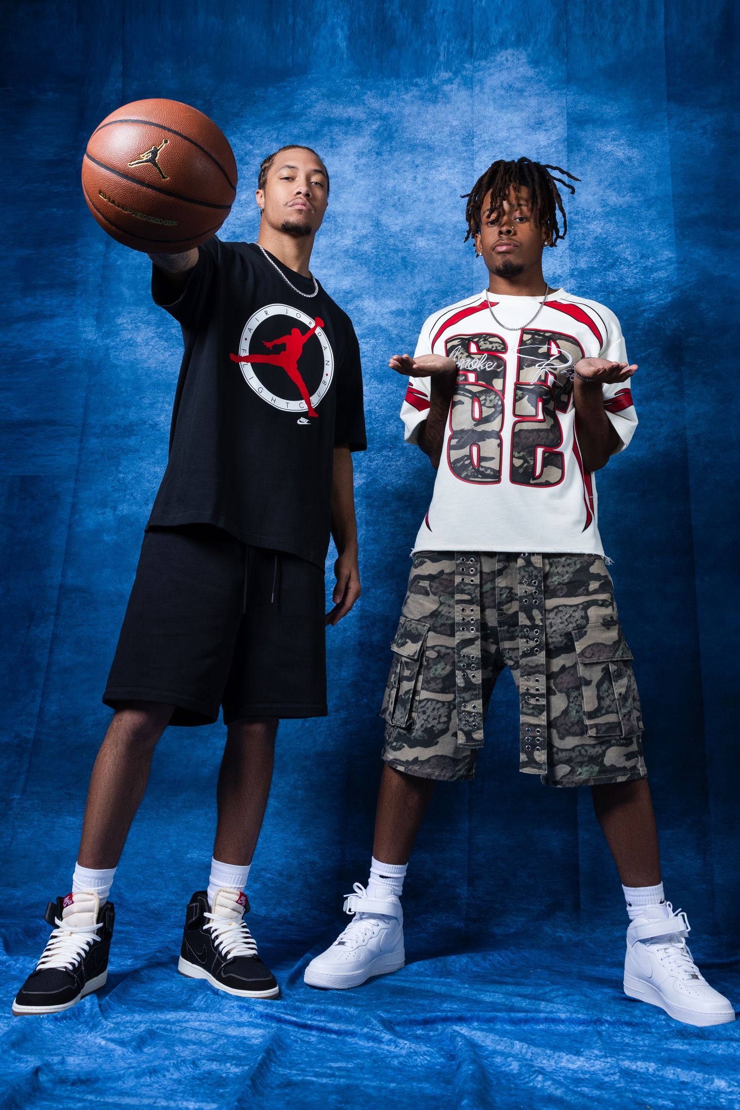 Two young men posing with a basketball in a studio, wearing Jordan brand and sports jerseys with cargo shorts.