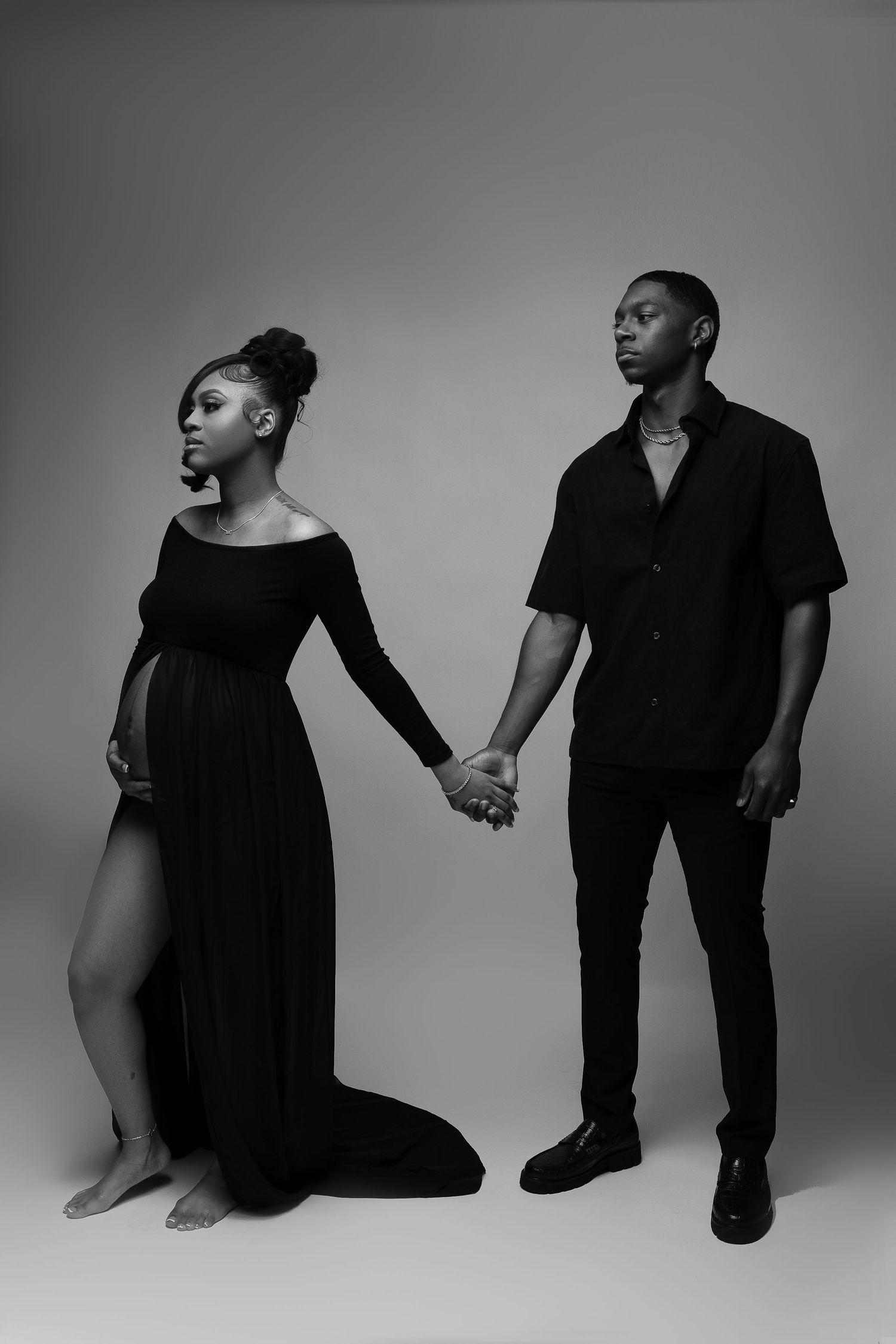 Artistic black and white maternity photo of couple holding hands in contrasting outfits.
