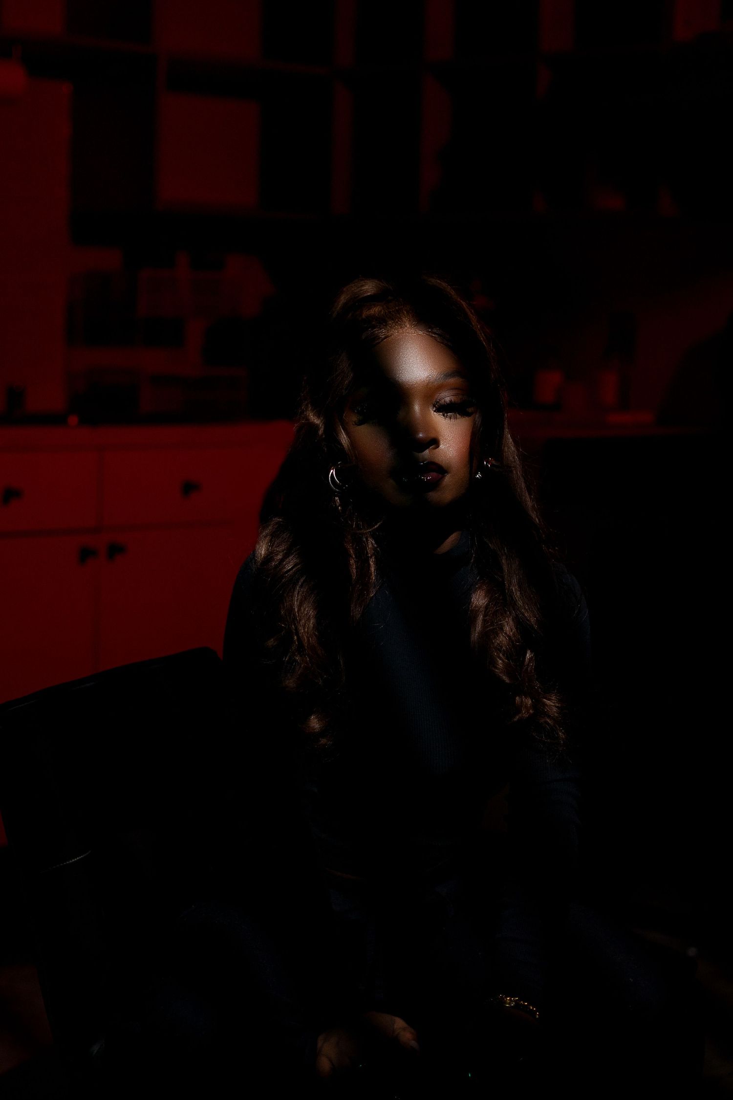Moody portrait in dark red lighting with long flowing hair and dramatic shadows.