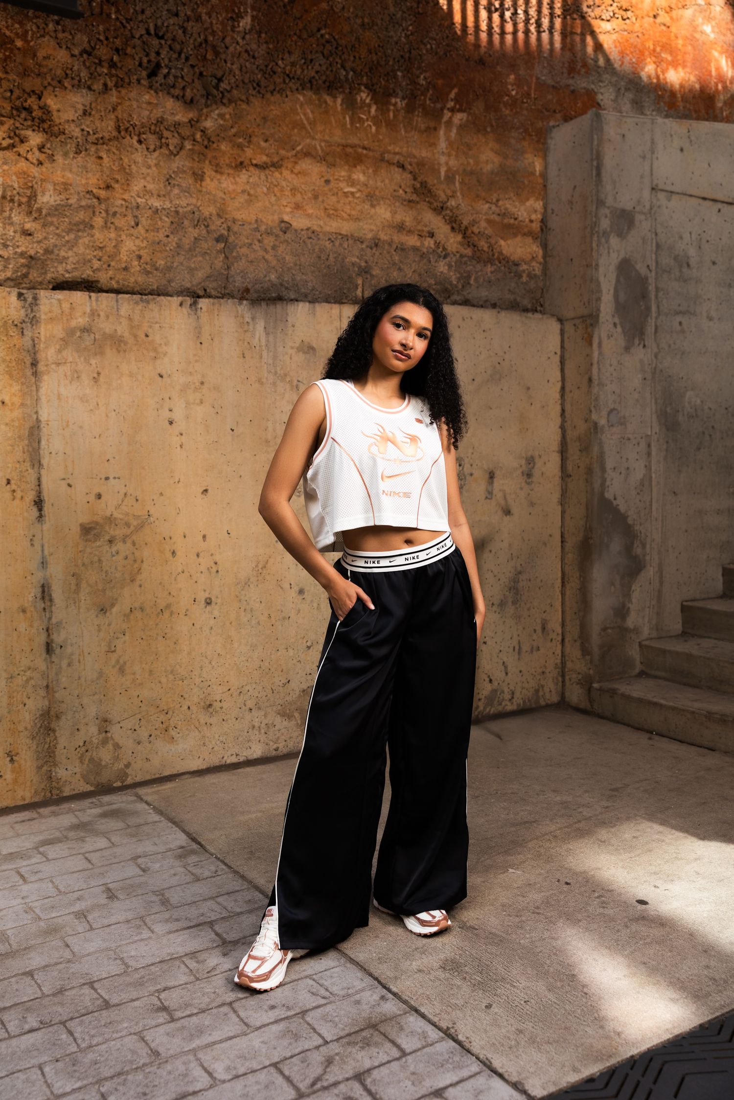 Athletic outfit featuring white Nike crop top and black wide-leg pants in an industrial setting.