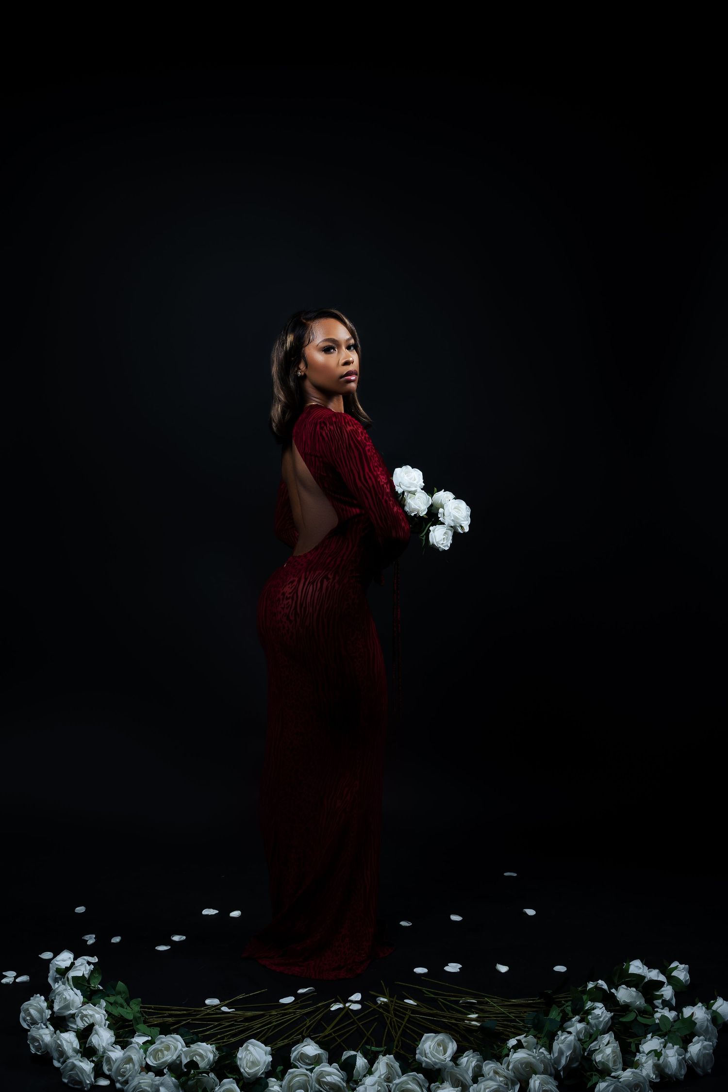 Artistic fashion photo with white roses surrounding a figure in a flowing red gown.