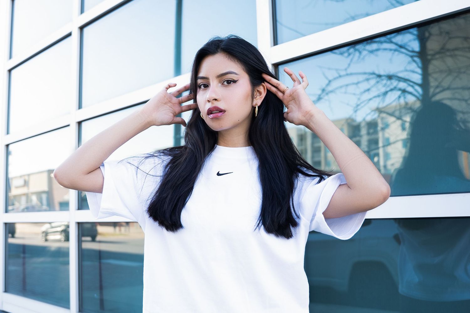 Fashion portrait showing person in white Nike shirt posing with hands in hair outdoors.