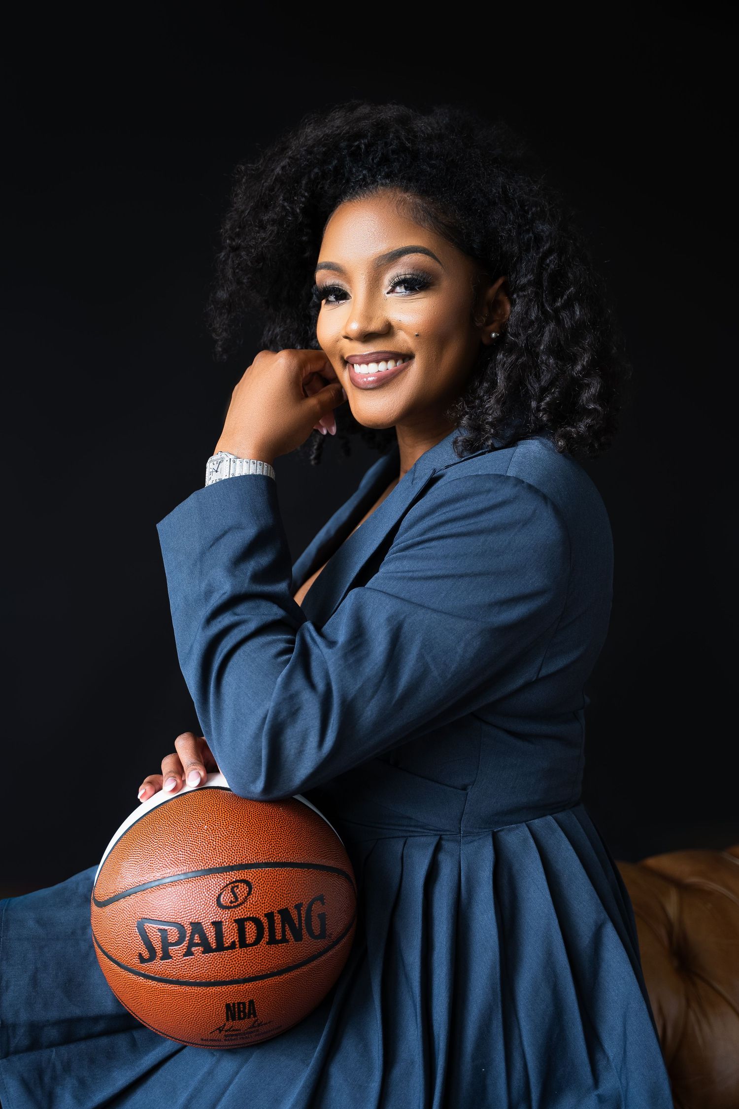 Elegant portrait pose with a Spalding basketball in a navy dress against dark backdrop.