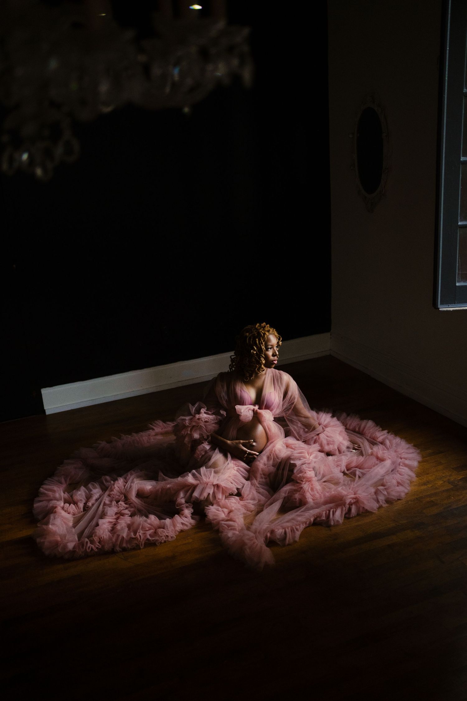 A series of dramatic photos featuring a flowing pink tulle dress in a dark room.