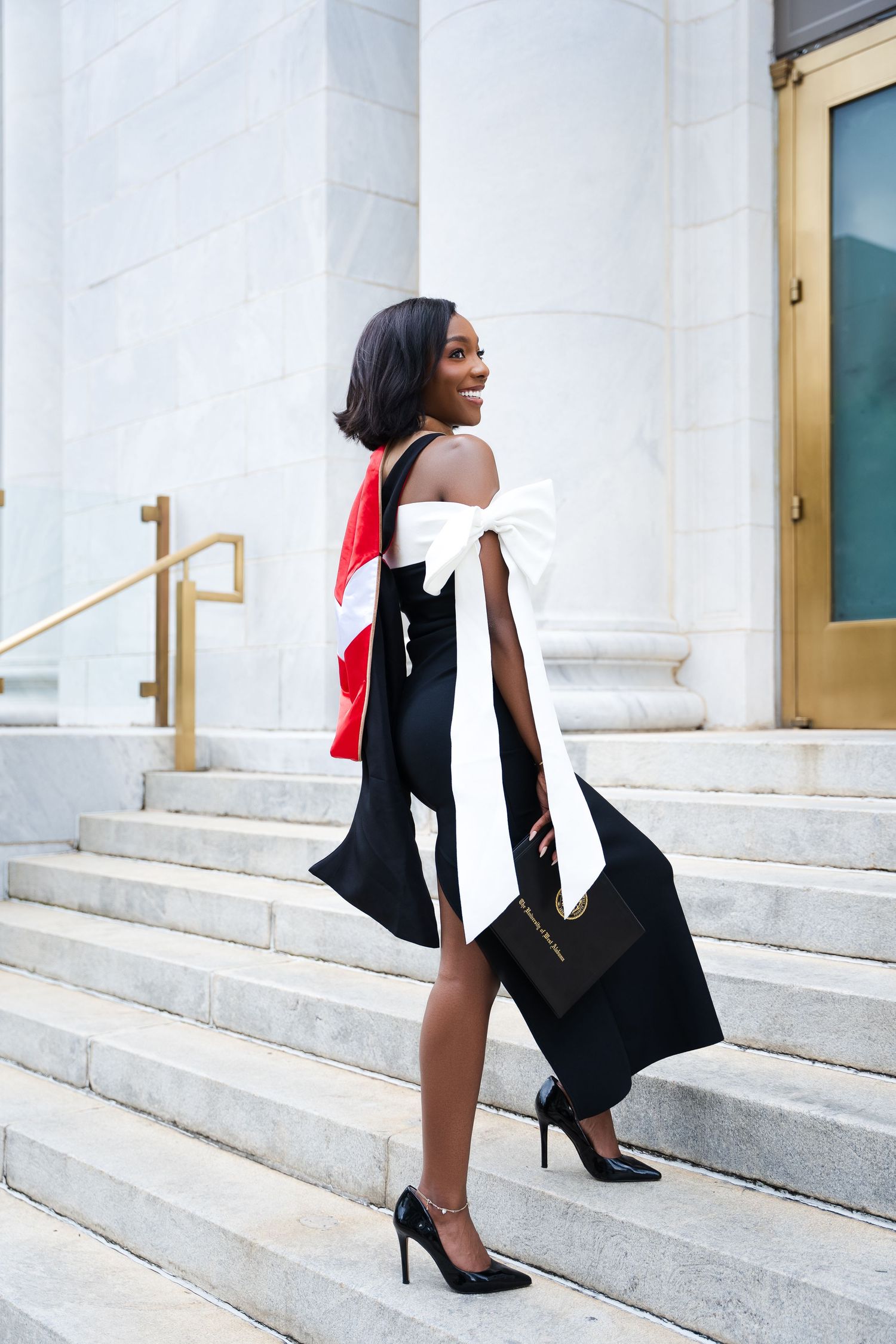 Stylish graduation photo on white marble steps with flowing black dress.