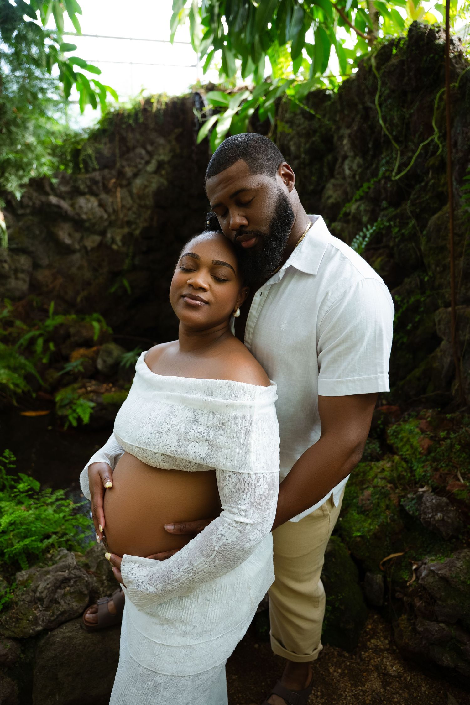 Maternity photoshoot in a lush garden setting with white lace dress and natural lighting.