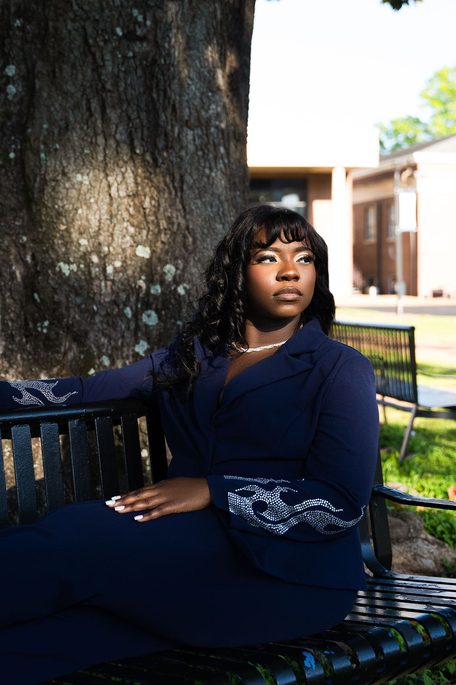 Person in navy blue outfit sitting on park bench near large tree trunk.