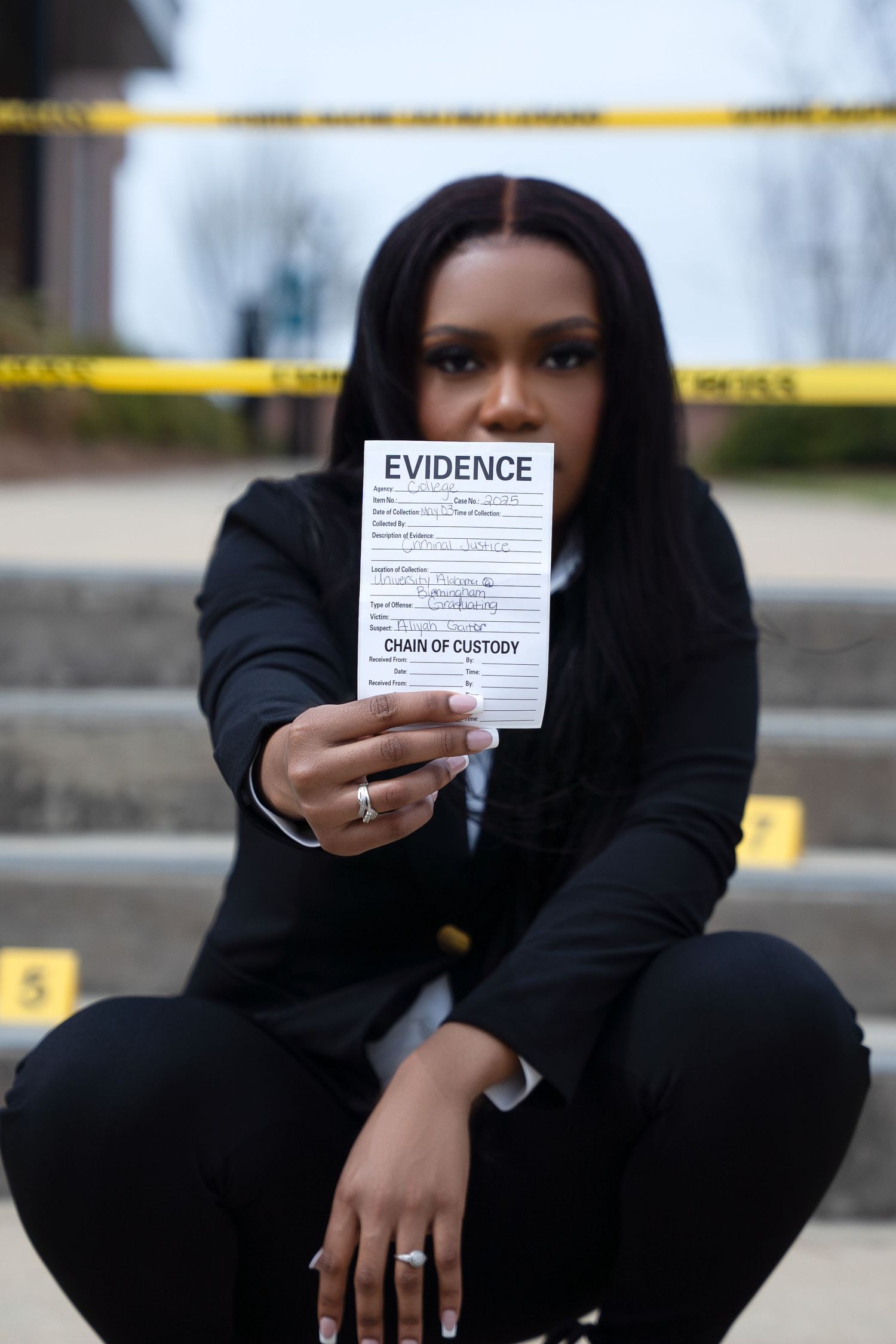 Person in black holds evidence tag at crime scene with yellow tape.