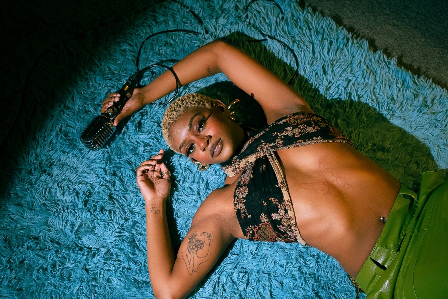 Person lying on blue carpet wearing patterned top.