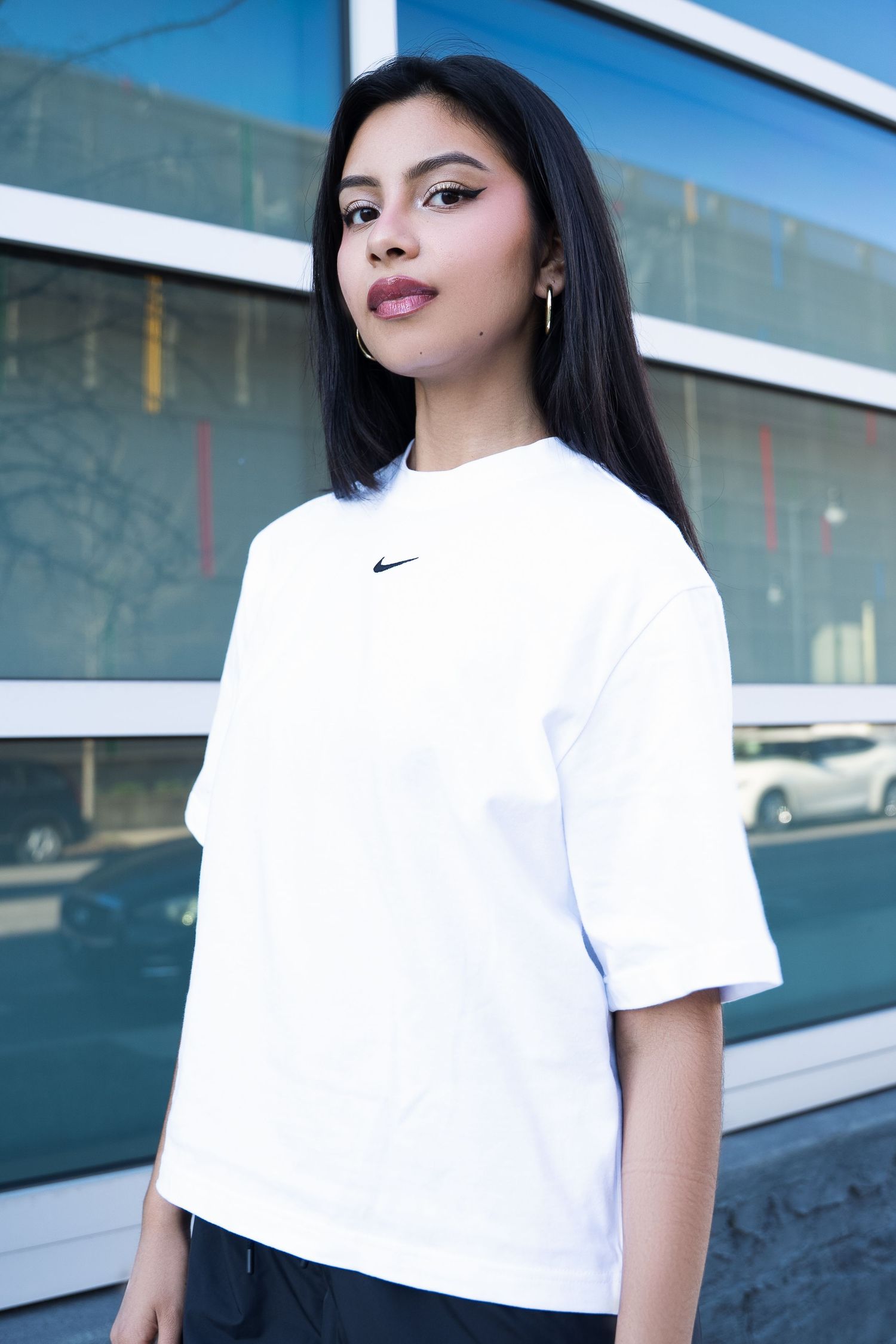 Simple portrait of person in white Nike t-shirt against modern glass building exterior.