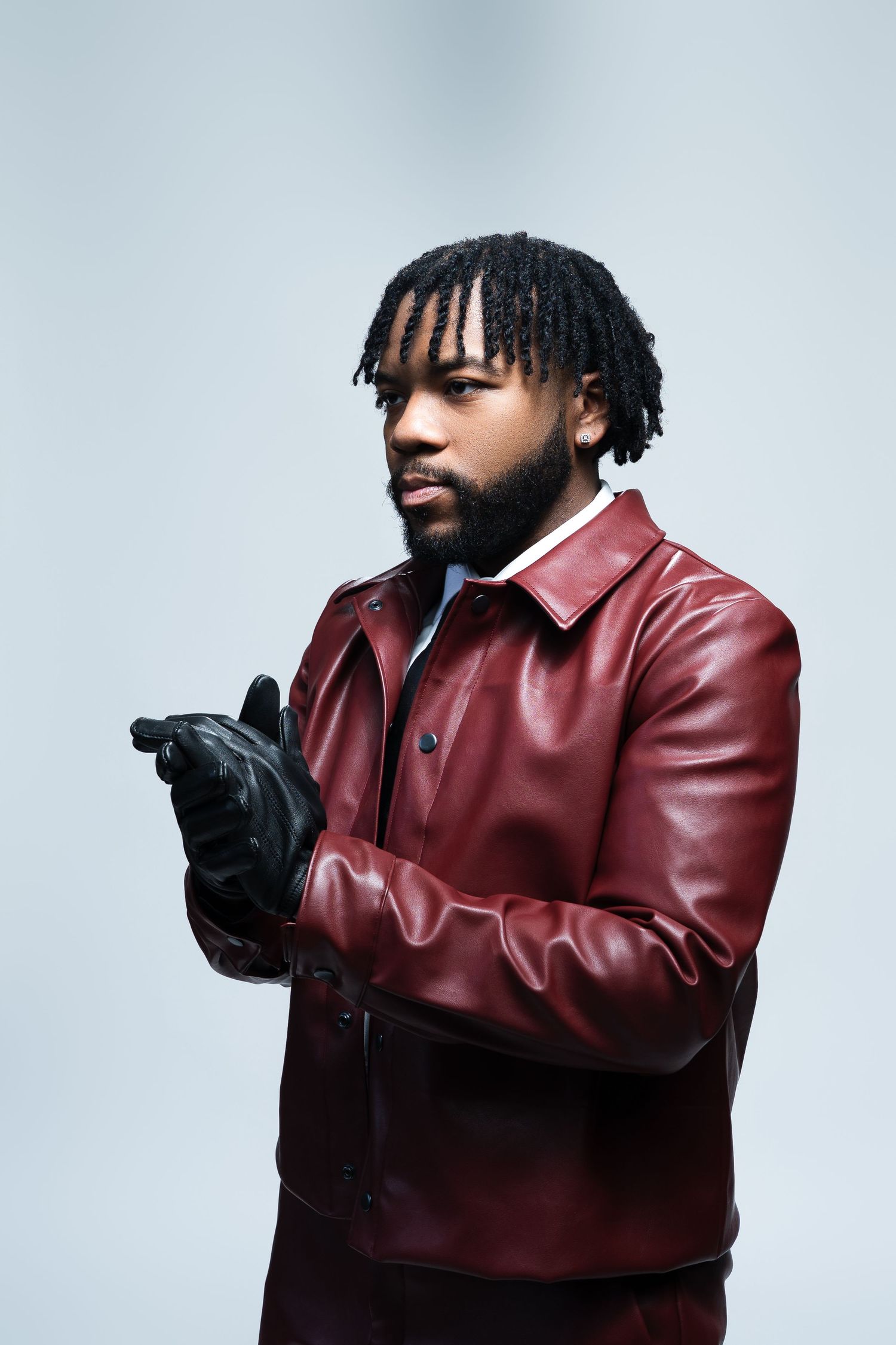 Stylish portrait of a person in burgundy leather jacket with black gloves against light background.